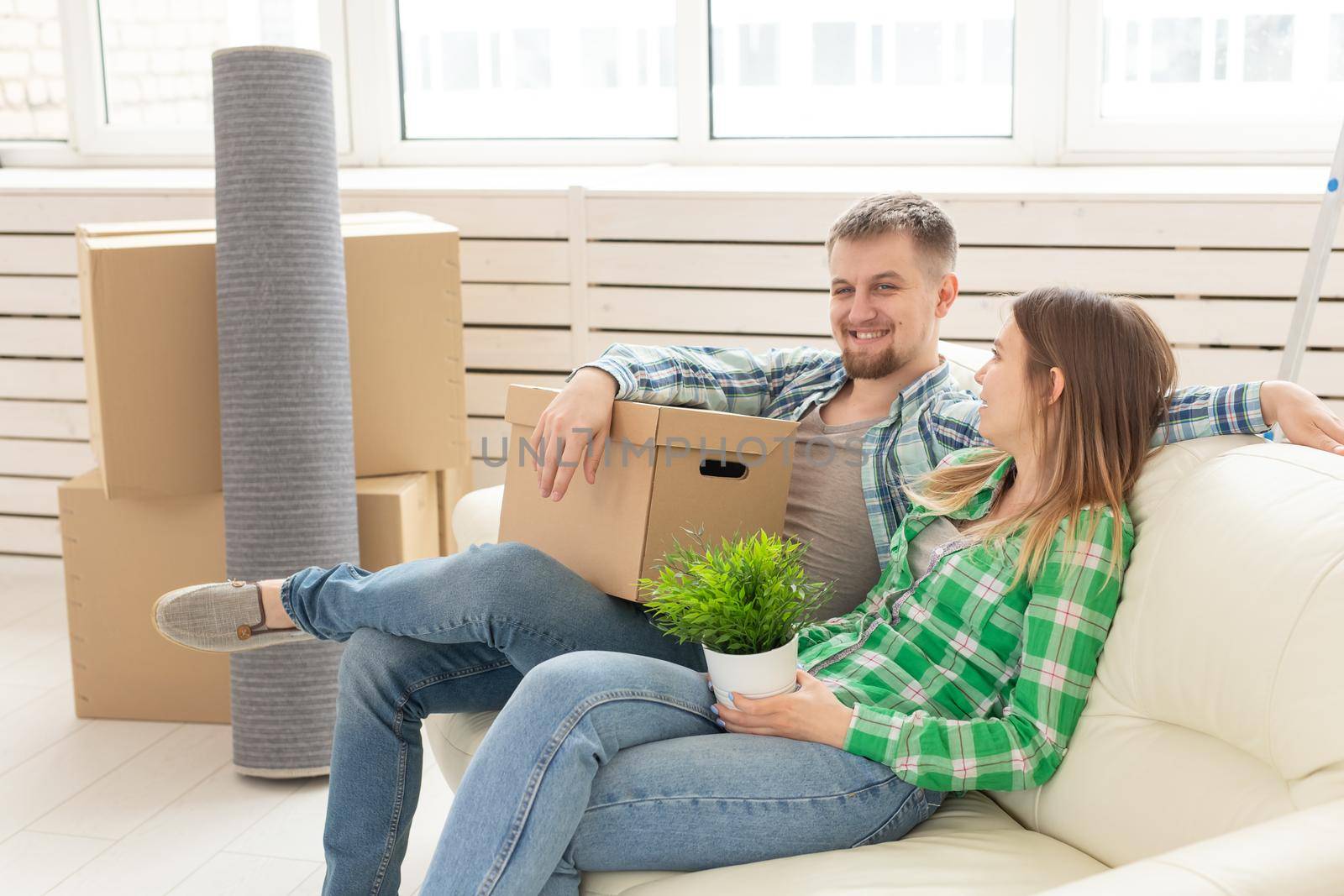 Positive cheerful couple rejoices in moving their new apartment sitting in the living room with their belongings. Concept of housewarming and mortgages for a young family. by Satura86