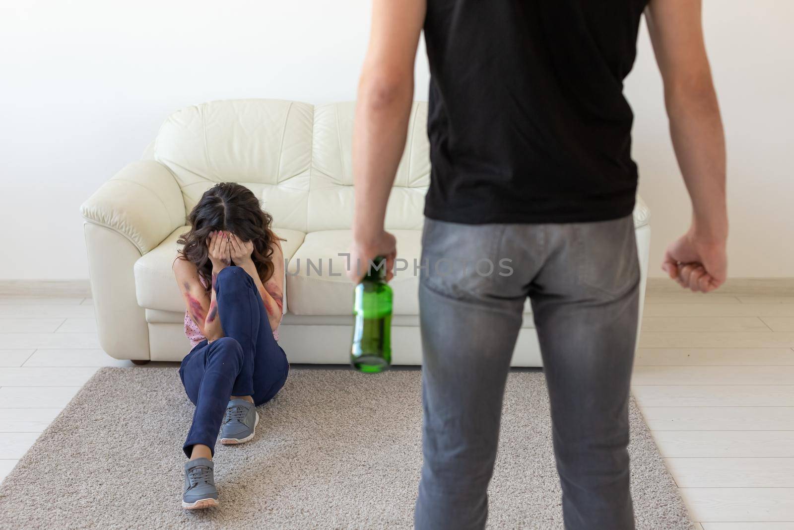 domestic violence, alcoholic and abuse concept - drunk man with bottle abusing his wife lying on the floor.