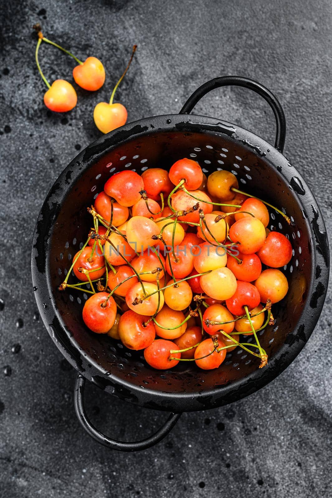 Yellow ripe cherries in a colander. Black background. Top view by Composter