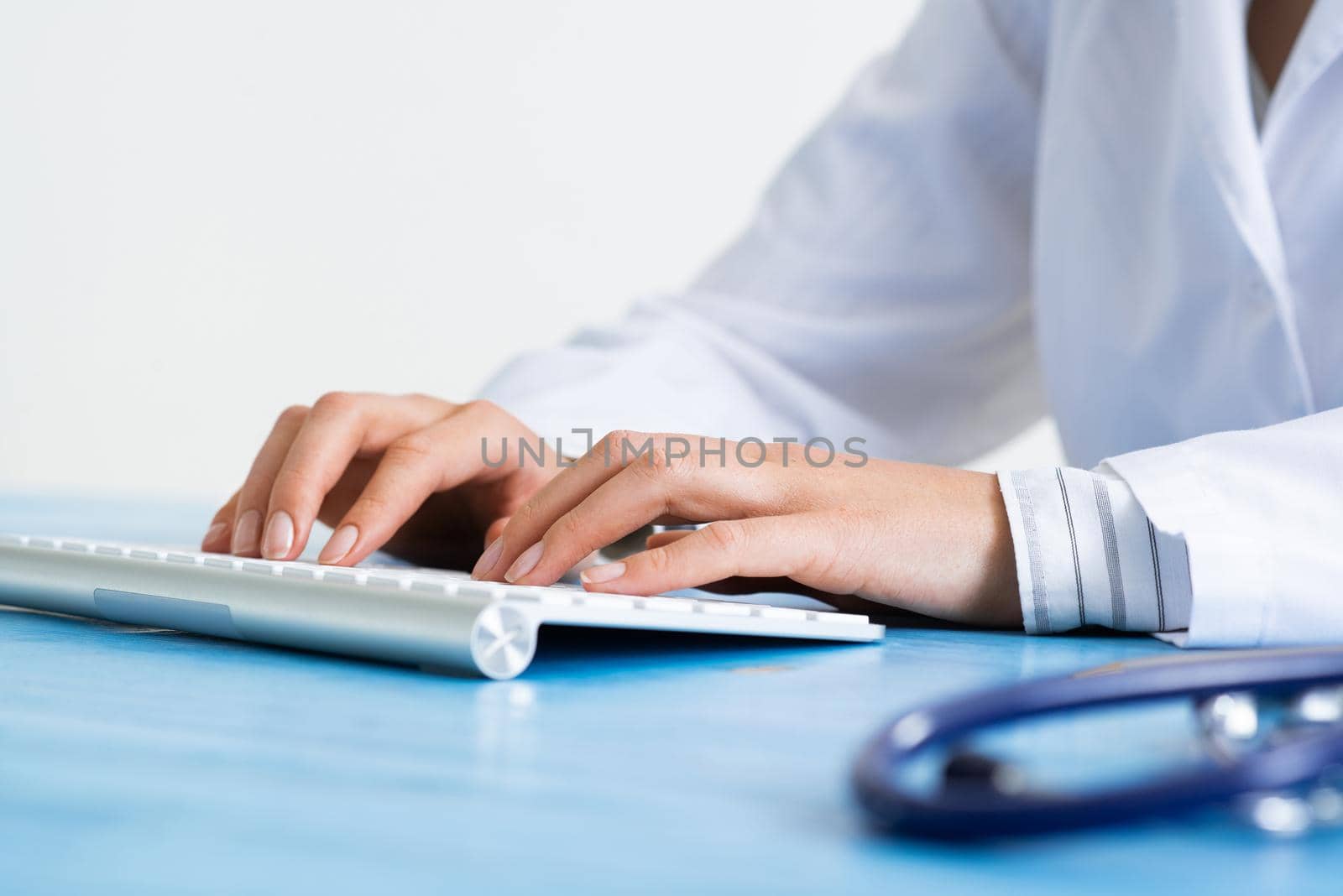 Doctor typing at computer keyboard. Physician in medical uniform working with computer at desk in office. Modern technology in examination and diagnosis. Doctor workplace with stethoscope.