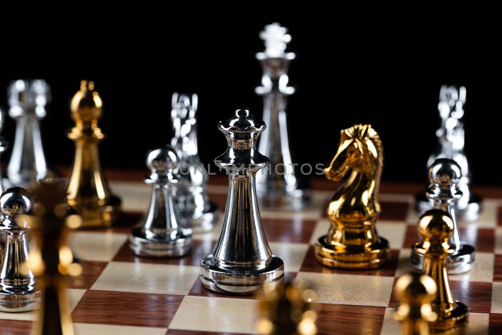 Gold and silver chess figures placed on wooden chessboard. Intellectual duel and tactical battle in business. Strategy planning, leadership and teamwork concept. Close-up metal chess pieces on board.