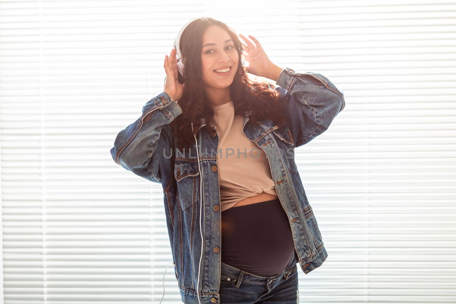 Young peaceful pregnant woman listens to pleasant classical music using smartphone and headphones. Concept of positive attitude before childbirth