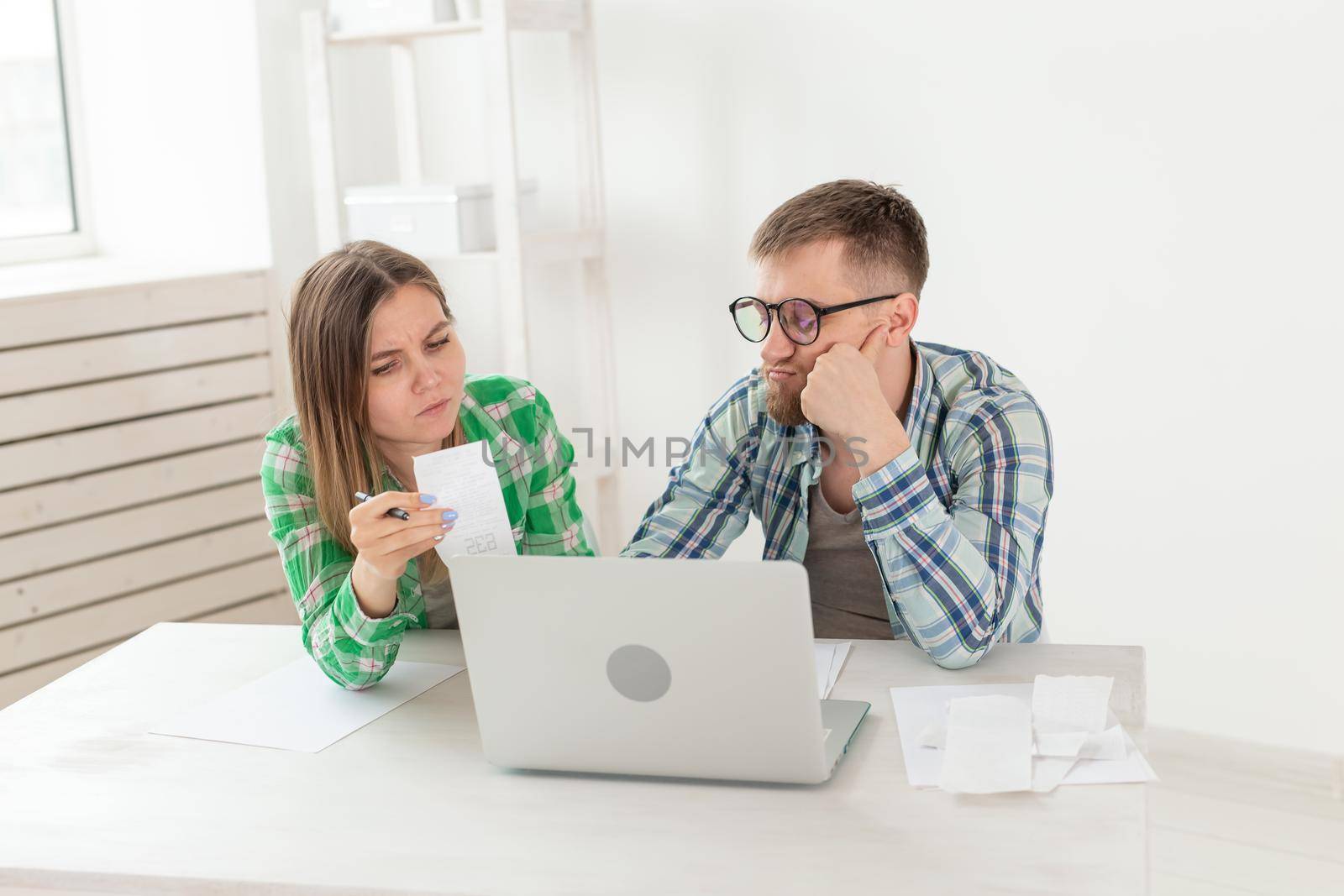 Husband and wife discuss amount in check for payment of the apartment and compare it with the rates on official website while sitting at the table with laptop. Concept of payment of utility bills