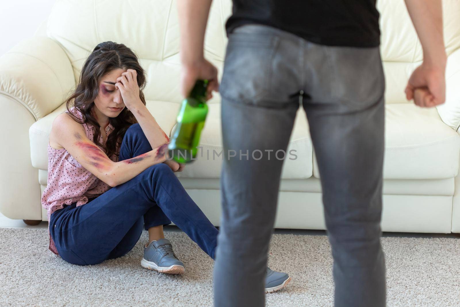 Victim, domestic violence, abuse and alcoholic concept - drunk man with bottle near his wife lying on the floor.