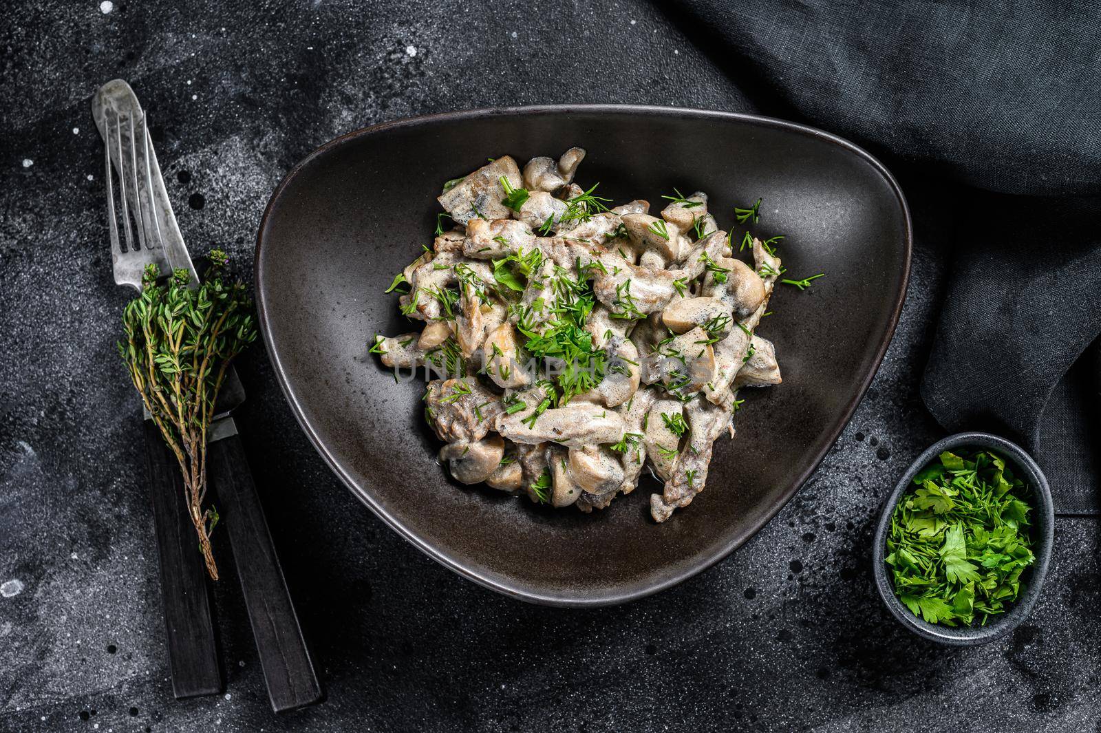 Beef stroganoff with mushrooms in a plate with cremini and champignons. Black background. Top view by Composter