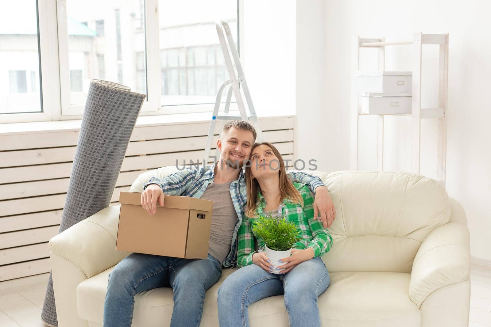 Positive young couple in love husband and wife are sitting on the couch in the new living room during the move and enjoy their new home. Mortgage concept and moving to a new home