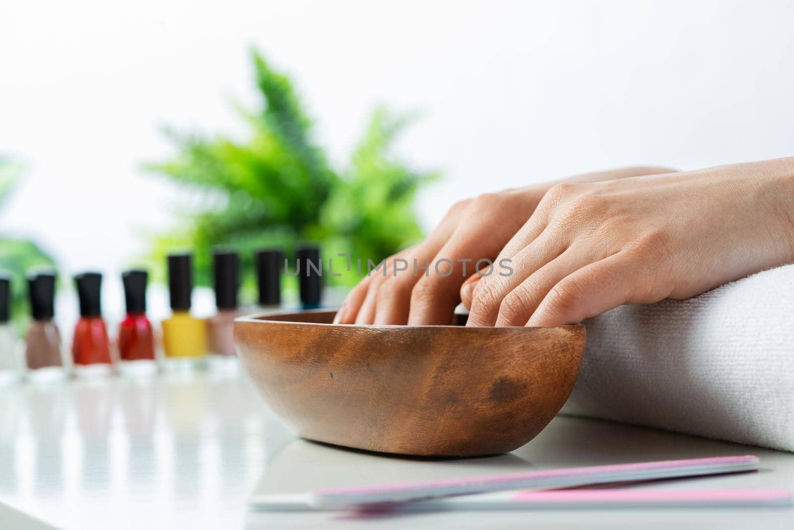 Closeup female hands in wooden bowl with water. Spa procedure and relaxation. Female hands preparing for manicure. Professional nail care and beautician service. Beauty and hygiene concept