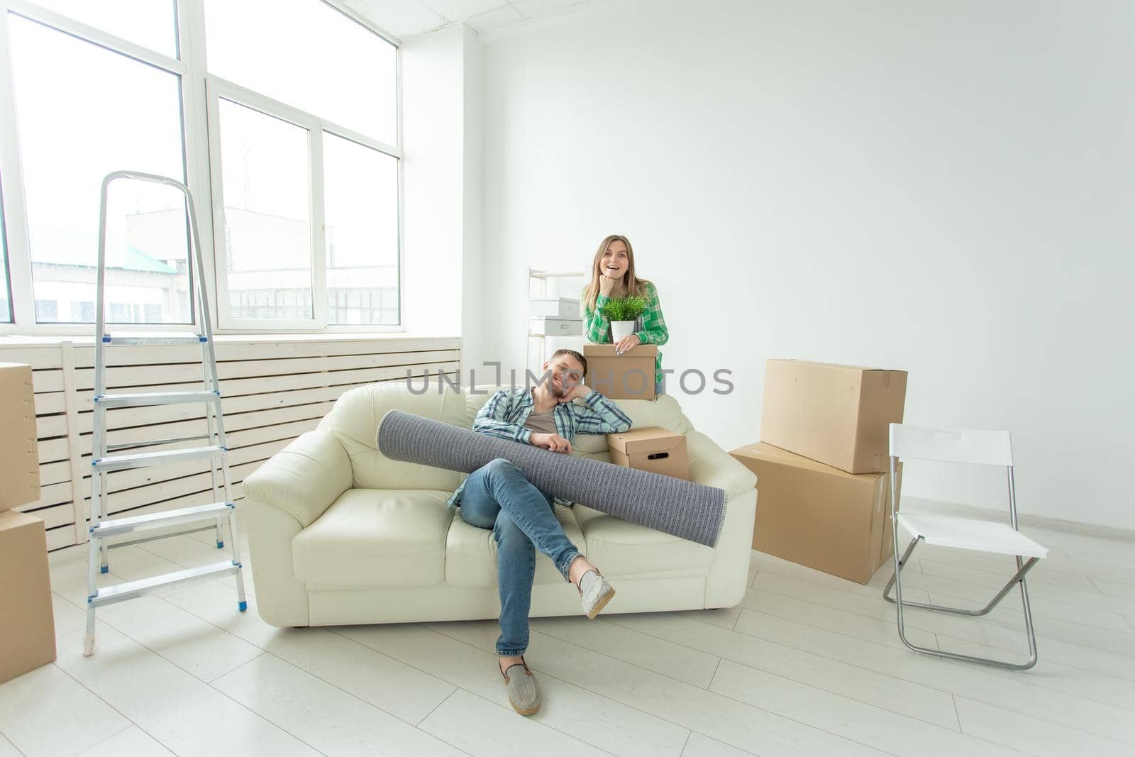 Satisfied cheerful young couple strong man and pretty woman holding their things in their hands sitting in the living room of a new apartment. Housewarming concept