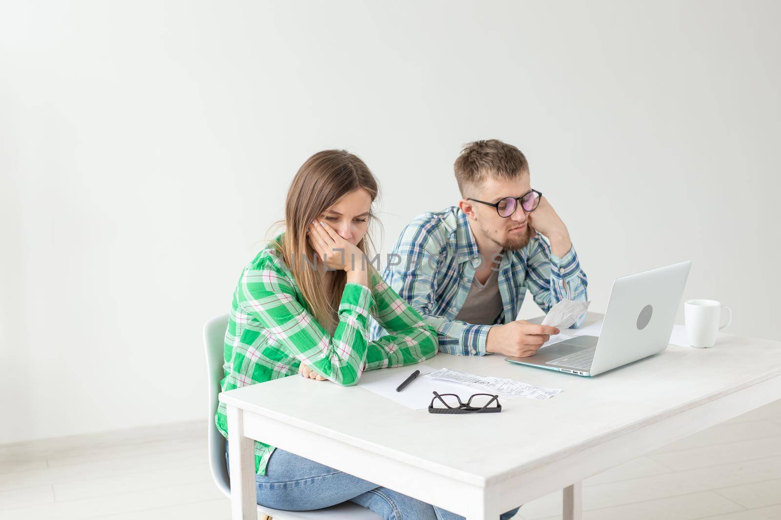 Dissatisfied young husband and wife recount utility bills for payment of an apartment and write the results in a notebook and laptop in their home accounting. by Satura86