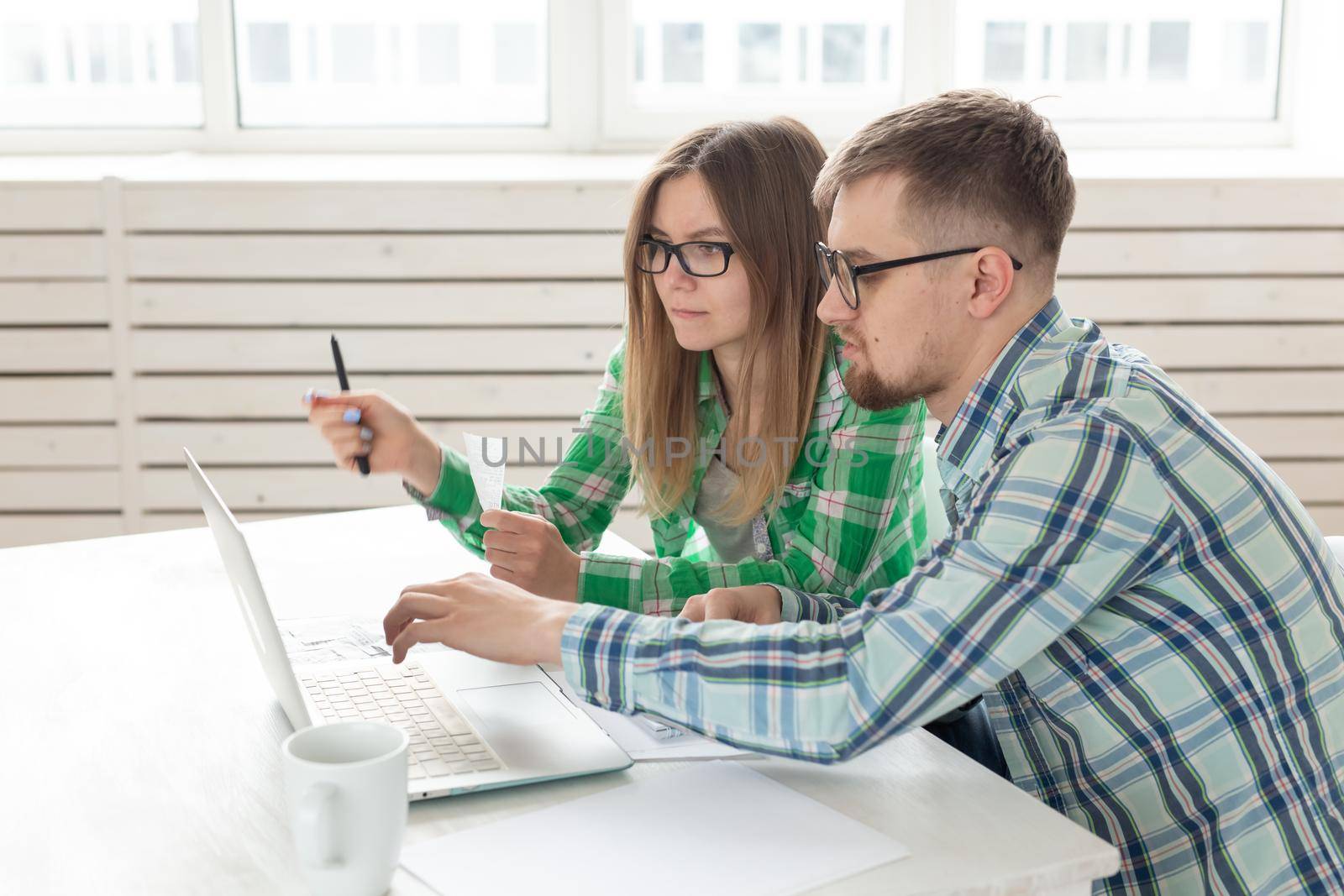 Dissatisfied young husband and wife recount utility bills for payment of an apartment and write the results in a notebook and laptop in their home accounting. by Satura86