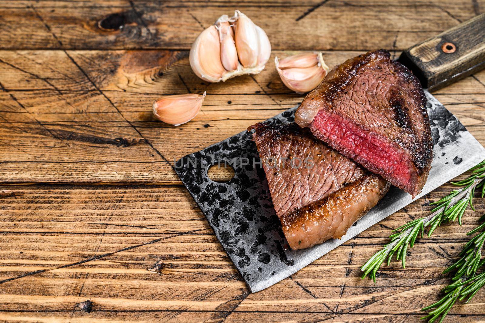 Grilled rump cap or brazilian picanha beef meat steak on a cleaver. wooden background. Top view. Copy space by Composter