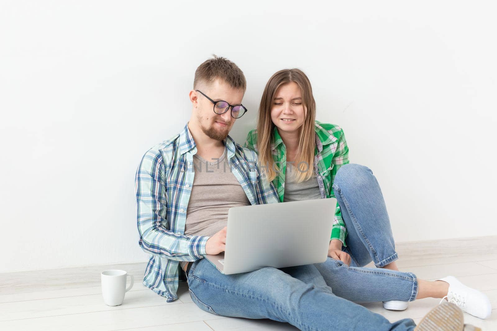 Charming young positive couple in casual clothes looking for an interior designer for their new apartment using a laptop and high-speed Internet. Apartment design concept. by Satura86