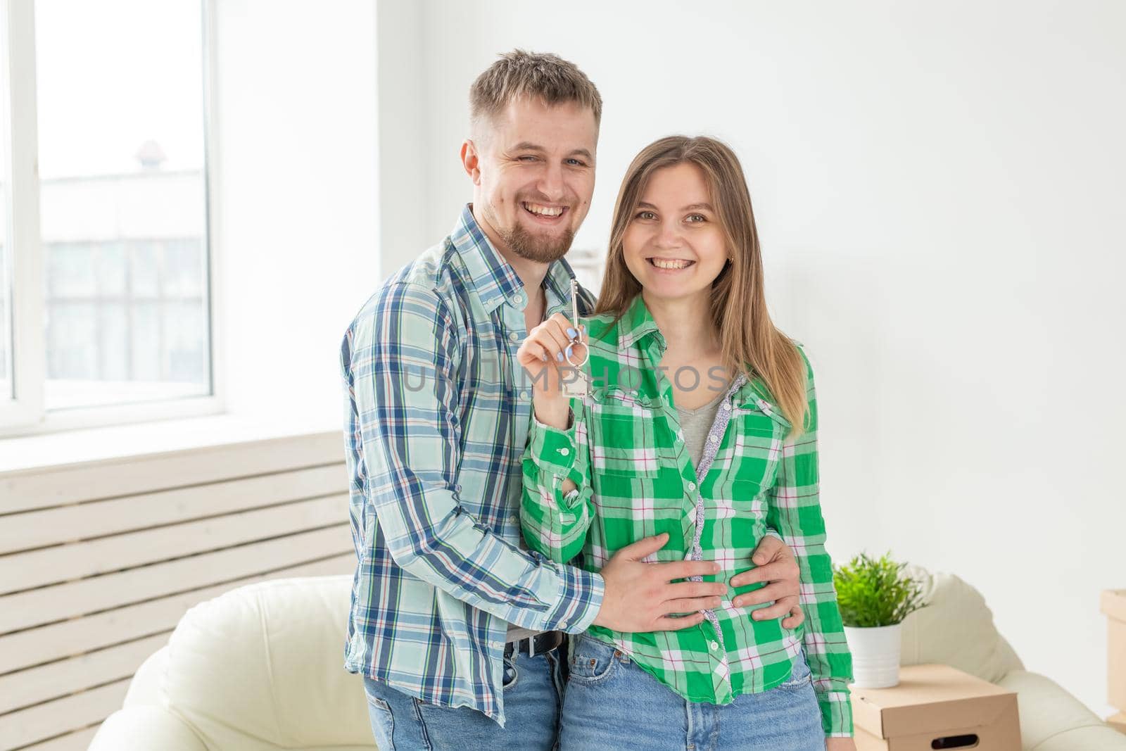 Charming young woman and her husband holding in hands the keys to their new apartment while sitting in her new living room. Housewarming and mortgage in new building concept by Satura86