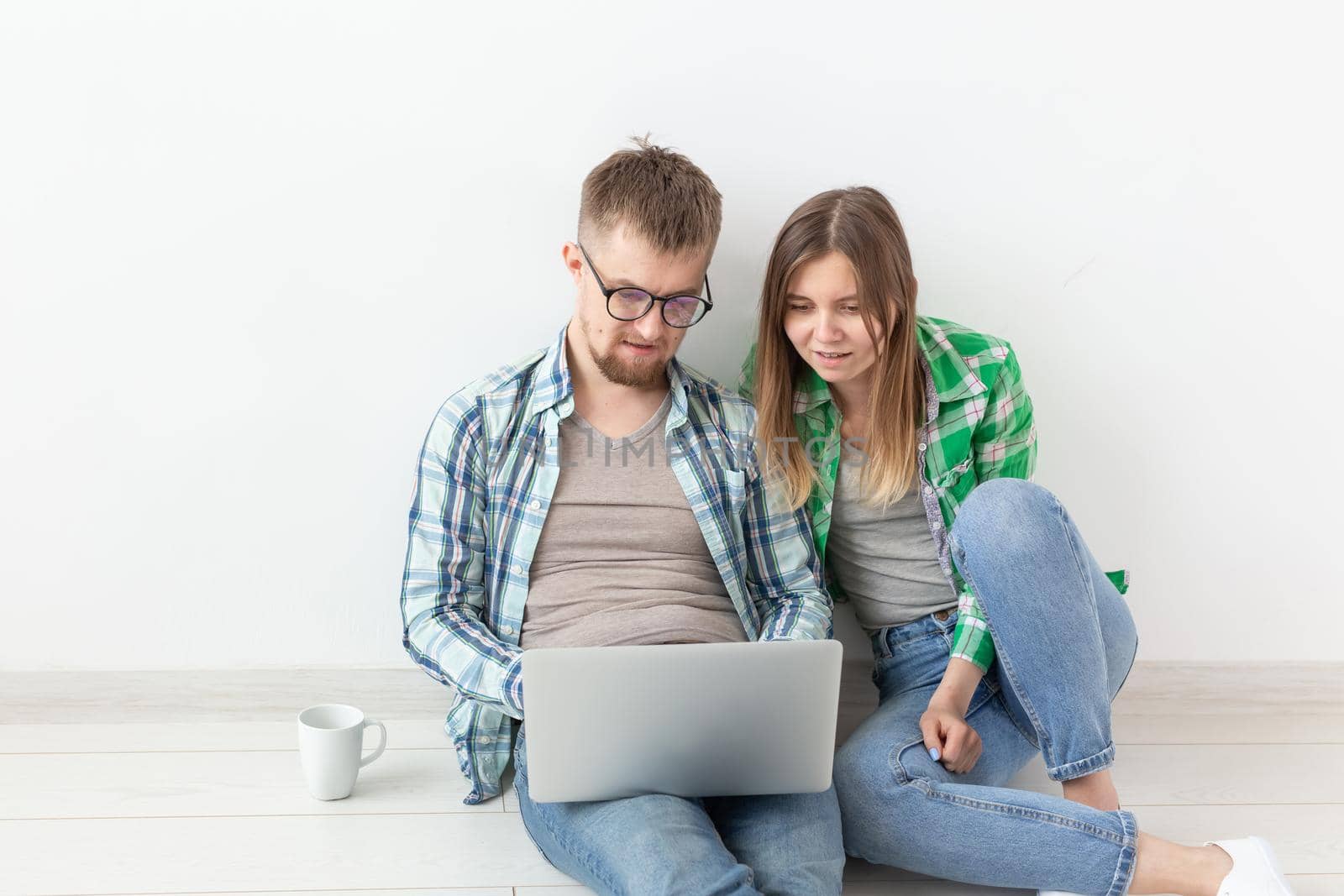 Charming young positive couple in casual clothes looking for an interior designer for their new apartment using a laptop and high-speed Internet. Apartment design concept. by Satura86