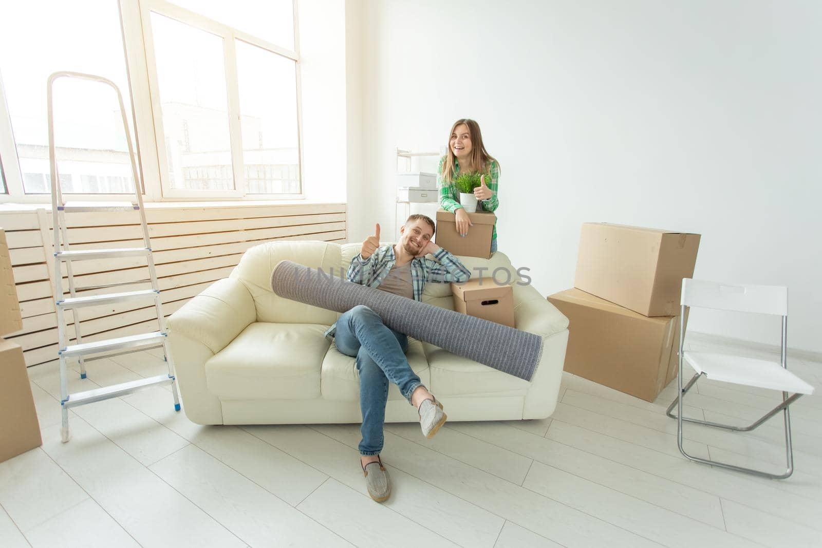 Satisfied cheerful young couple strong man and pretty woman holding their things in their hands sitting in the living room of a new apartment. Housewarming concept. by Satura86