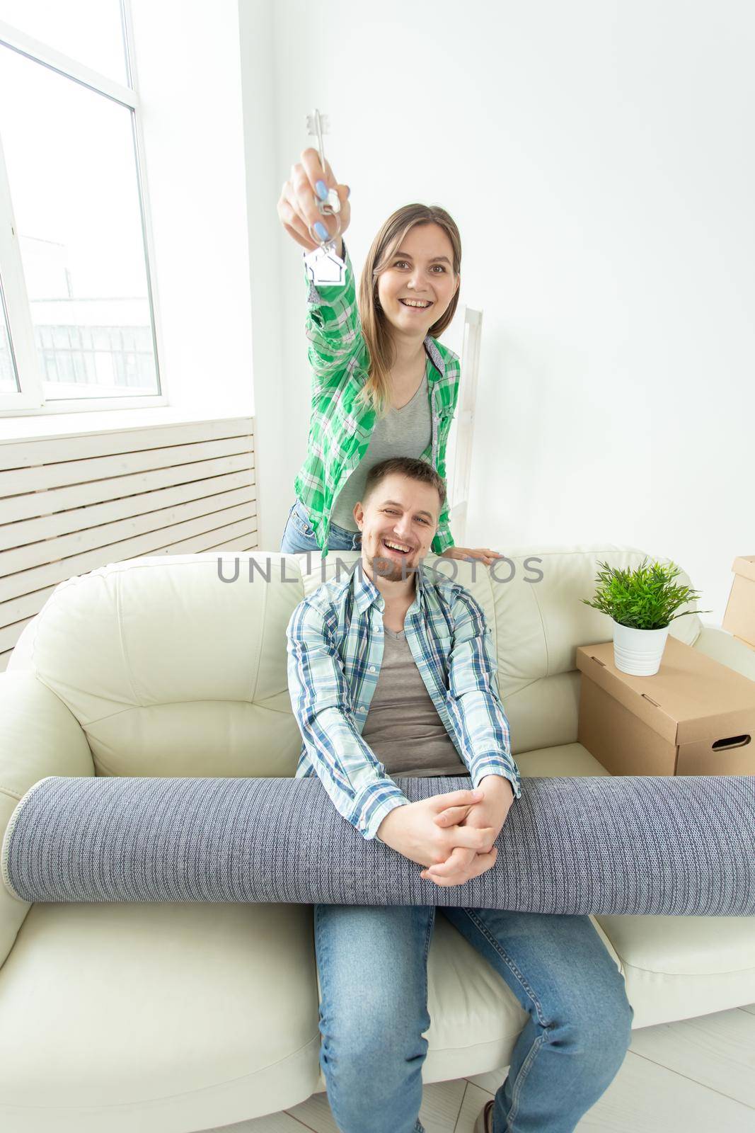 Funny young woman and her husband holding in hands the keys to their new apartment while sitting in her new living room. Housewarming and mortgage in new building concept by Satura86