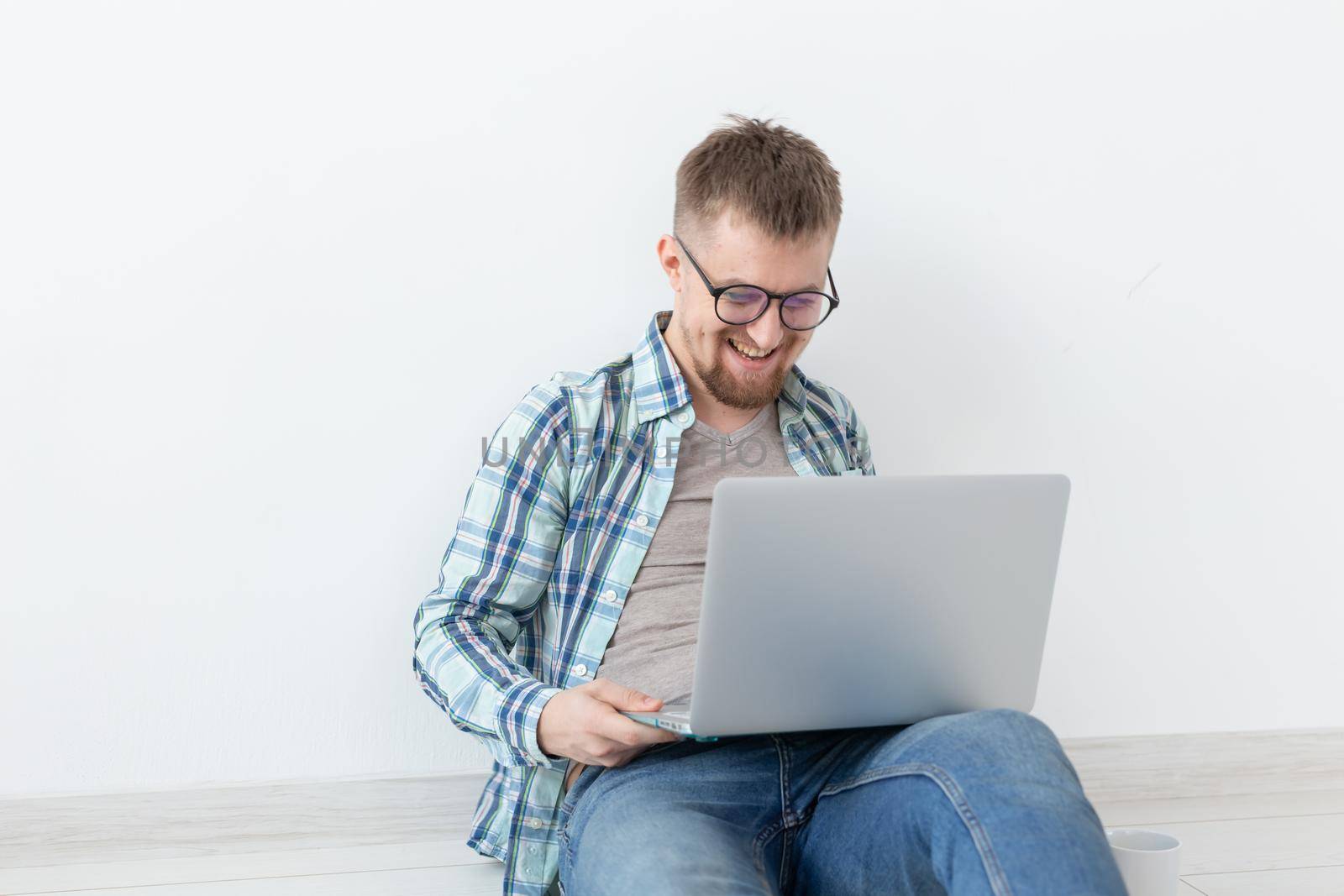 Positive young man in casual clothes and glasses surfing the Internet using Wi-Fi and a laptop in search of rental housing. Housewarming and apartment search concept. by Satura86