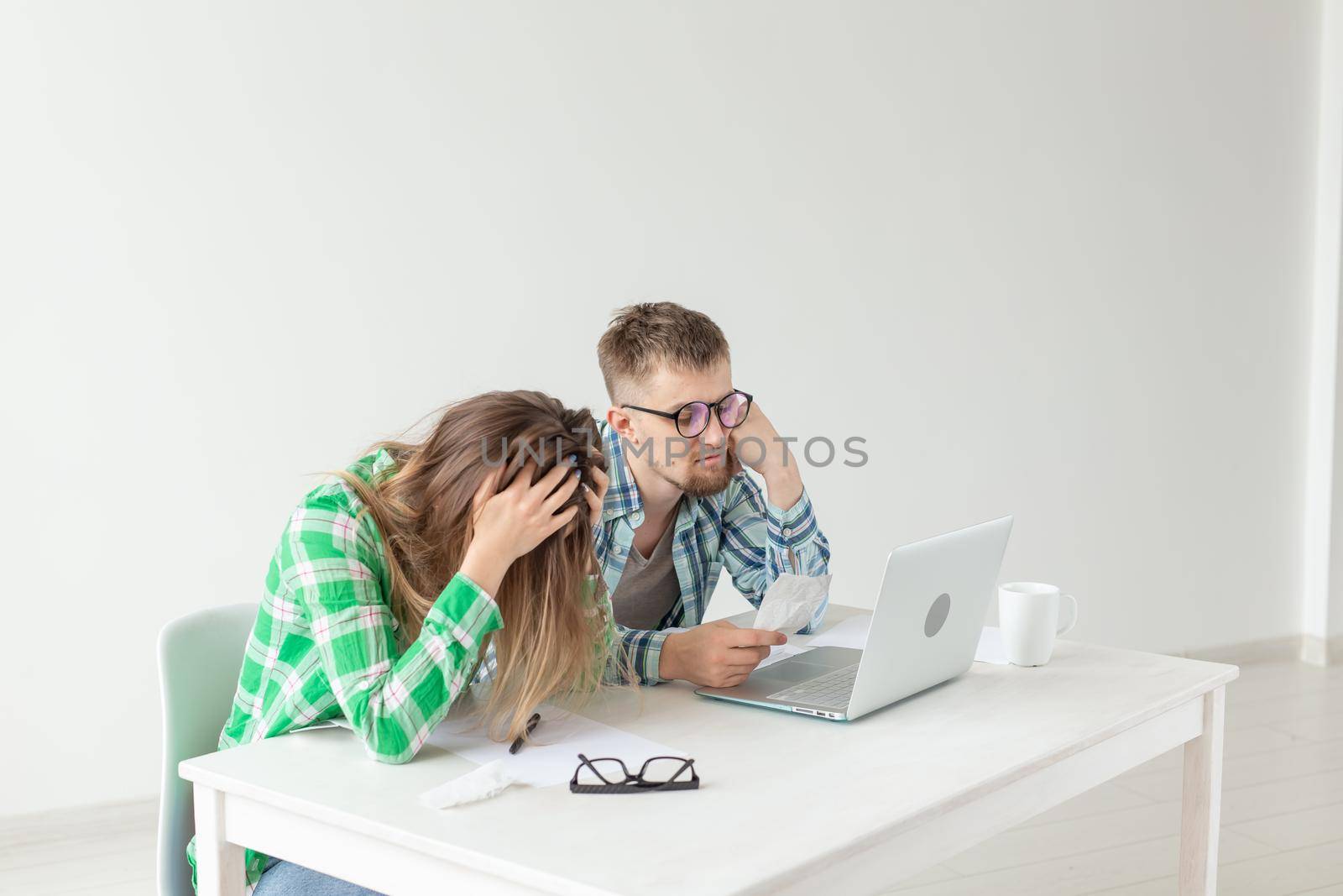 Young husband and wife are upset about numerous checks for payments and purchases for repairs while sitting at the table with a laptop. The concept of low living standards and savings. Copyspace