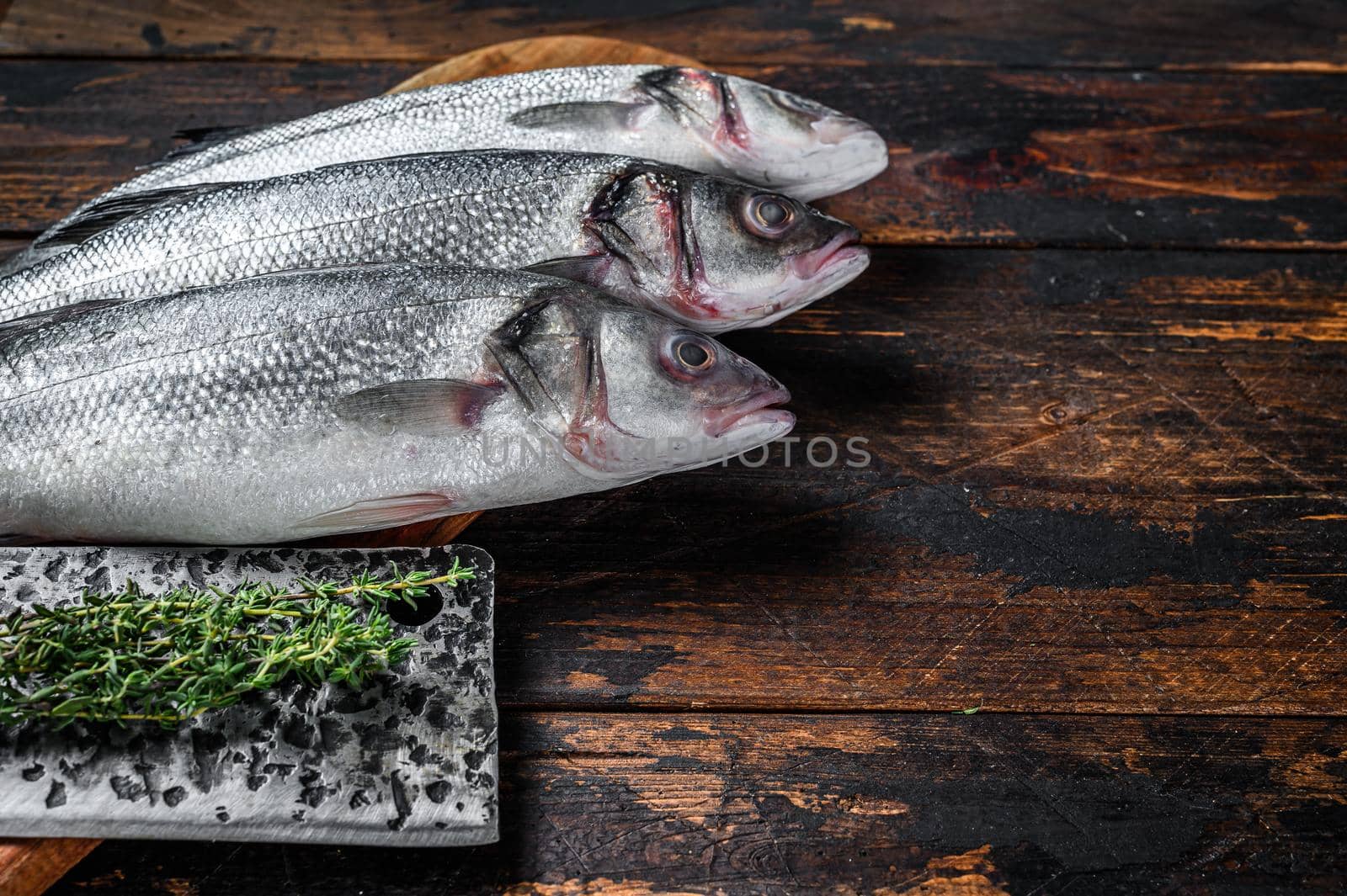 Fresh raw fish seabass on a cutting board. Dark wooden background. Top view. Copy space by Composter
