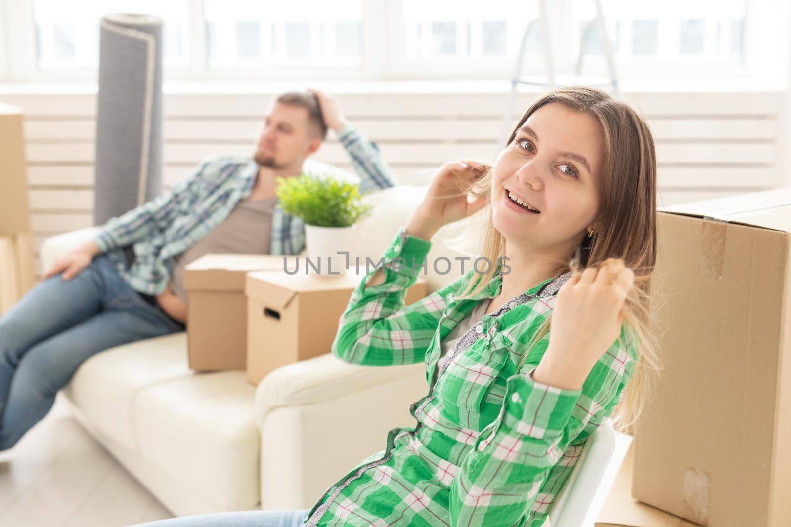 Positive smiling young girl sitting against her laughing blurred husband in a new living room while moving to a new home. The concept of joy from the possibility of finding new housing. by Satura86