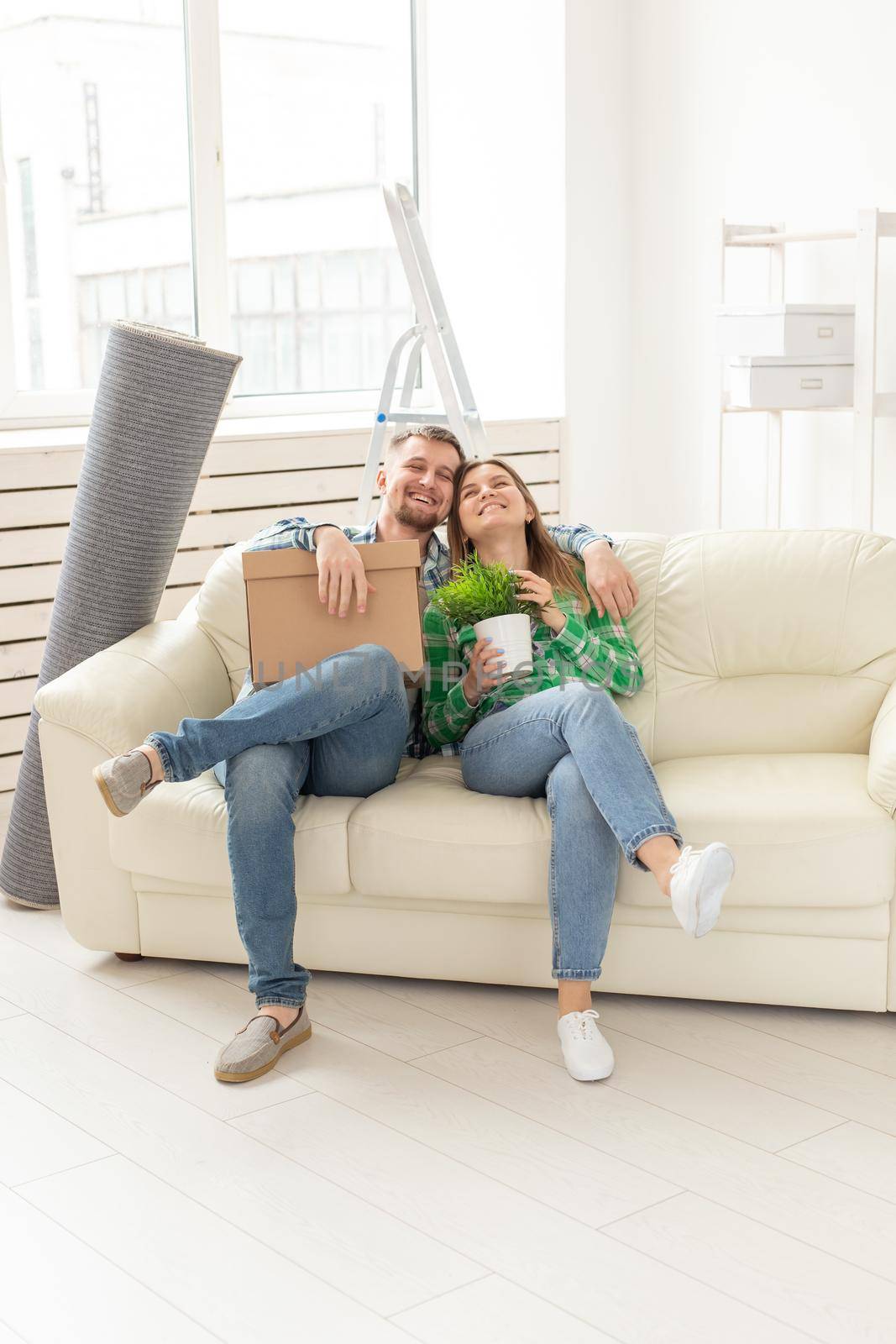 Positive young couple in love husband and wife are sitting on the couch in the new living room during the move and enjoy their new home. Mortgage concept and moving to a new home