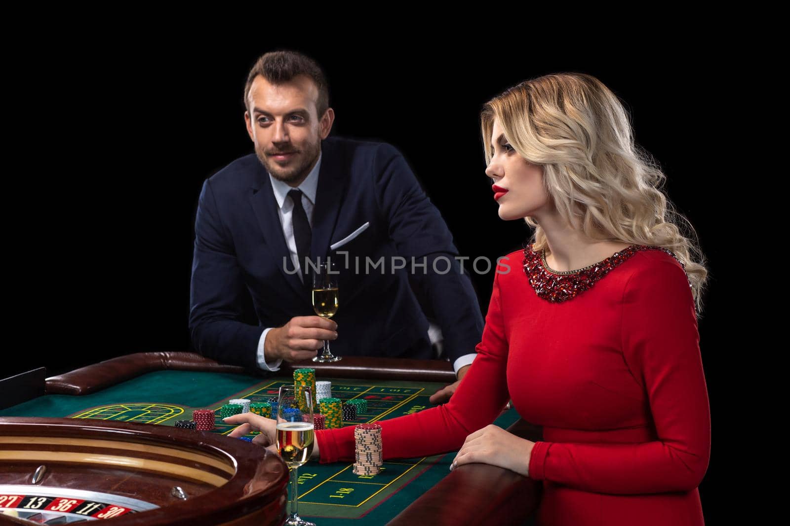 A beautiful young woman and a man are sitting at a roulette table. Casino. Black background. Excitement. Risk. Luck
