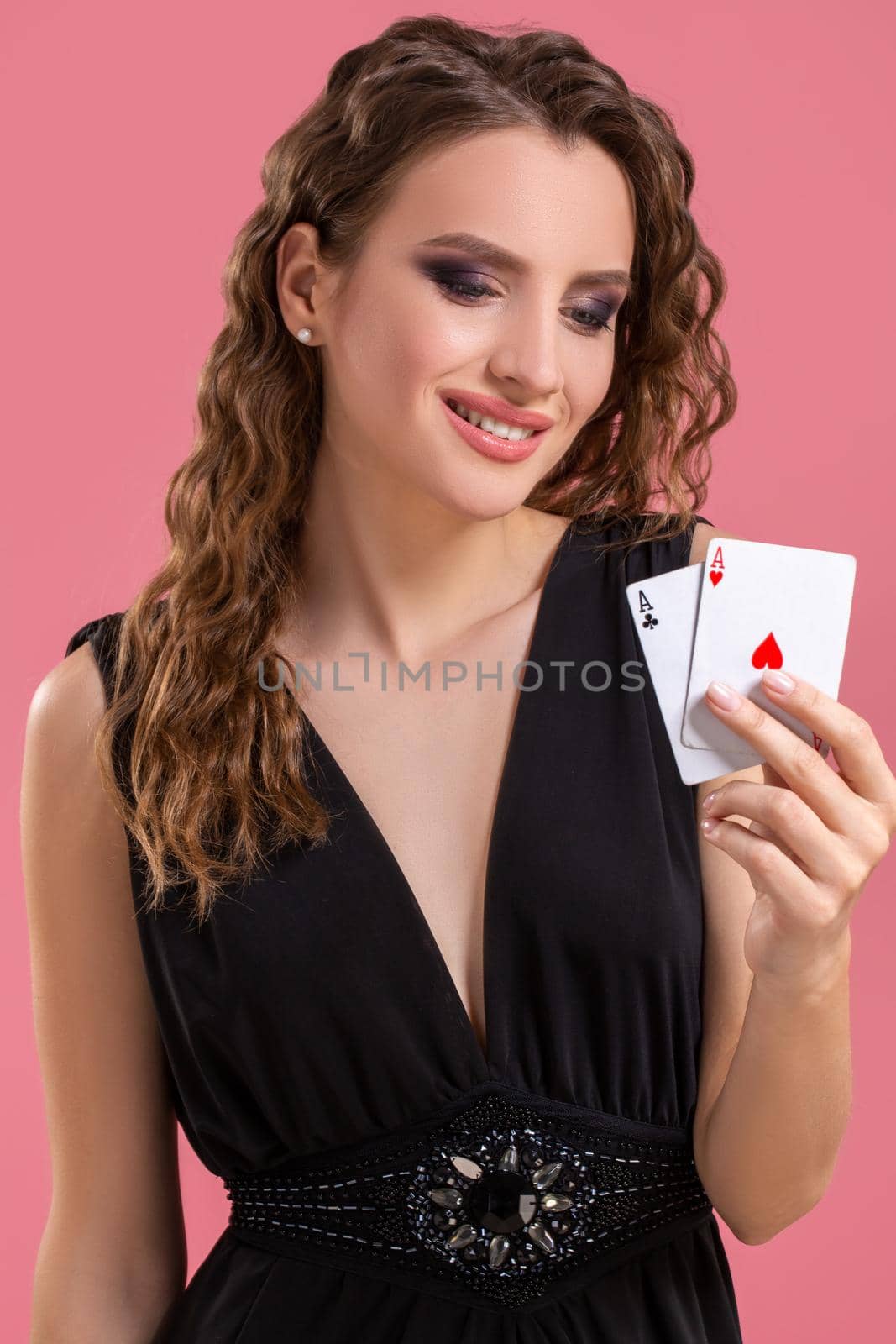 Young woman in black dress holding two aces in hand against on pink background. Studio shot