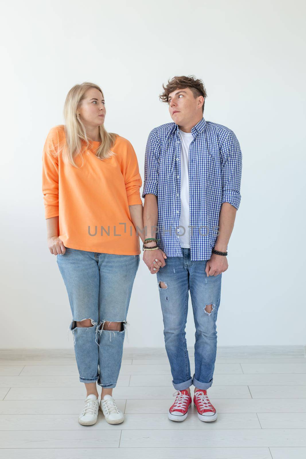 Young funny couple charming serious girl and a crazy young guy in casual clothes holding hands and posing on a white background. Misunderstandings in the relationship concept. Copyspace