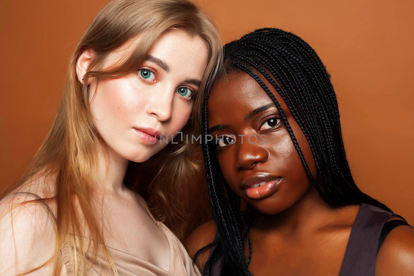 two pretty girls african and caucasian blond posing cheerful together on brown background, ethnicity diverse lifestyle people concept close up