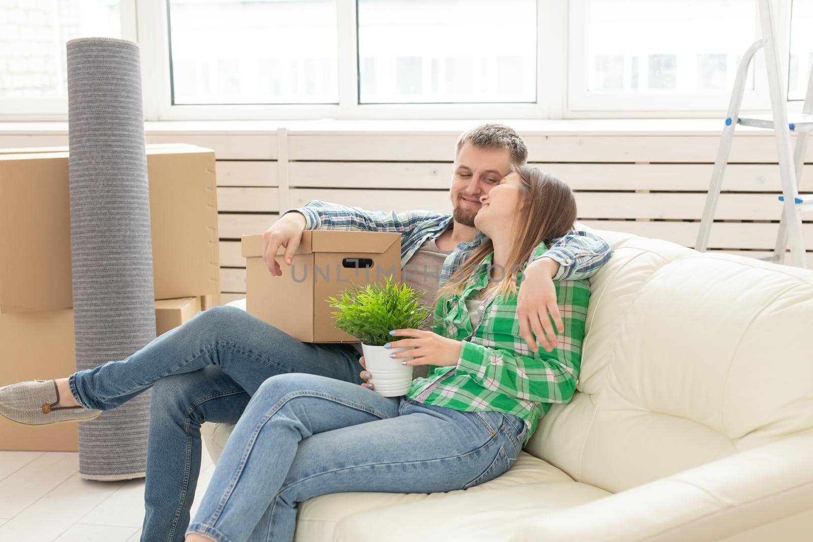 Positive young couple in love husband and wife are sitting on the couch in the new living room during the move and enjoy their new home. Mortgage concept and moving to a new home. by Satura86