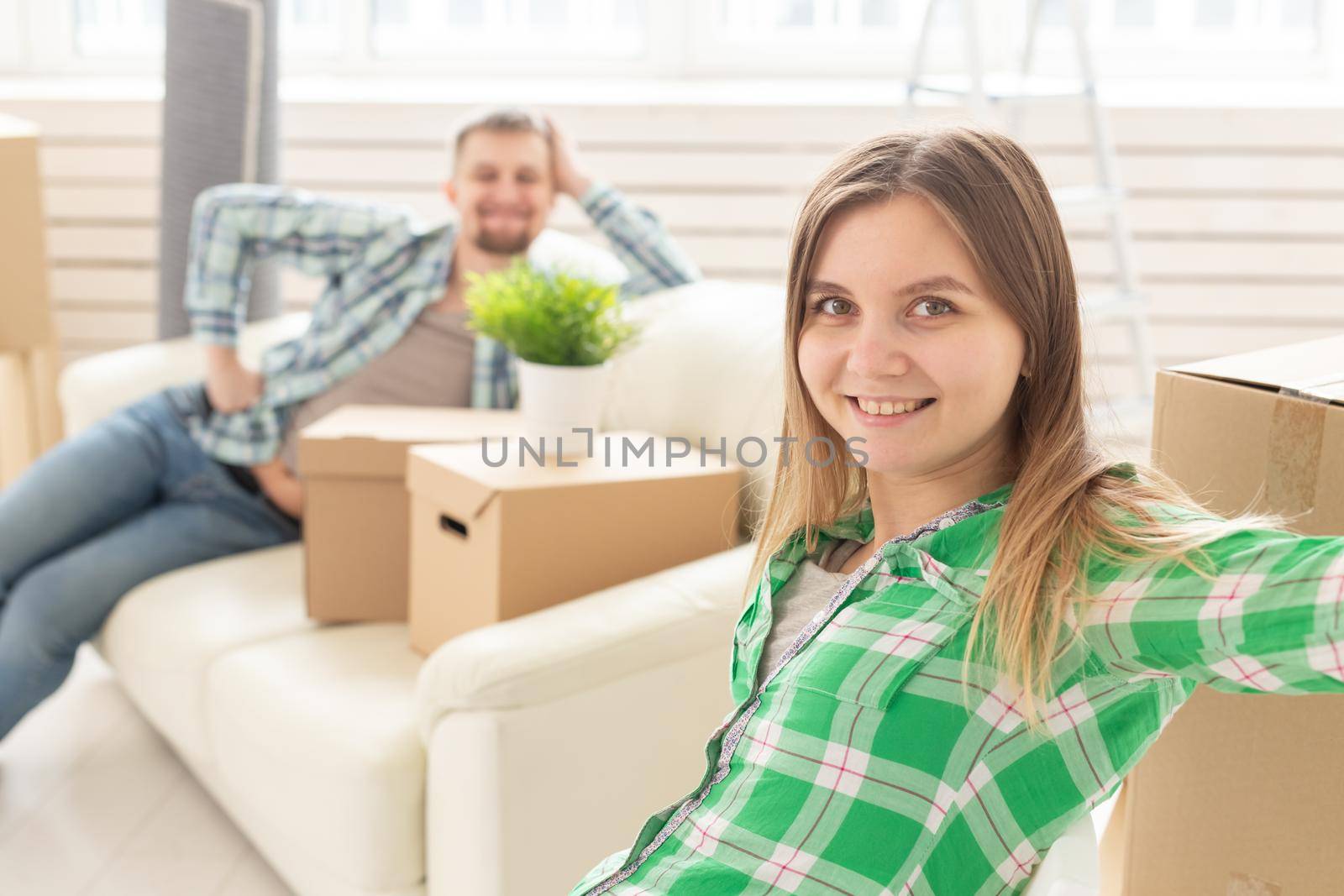 Positive smiling young girl sitting against her laughing blurred husband in a new living room while moving to a new home. The concept of joy from the possibility of finding new housing. by Satura86