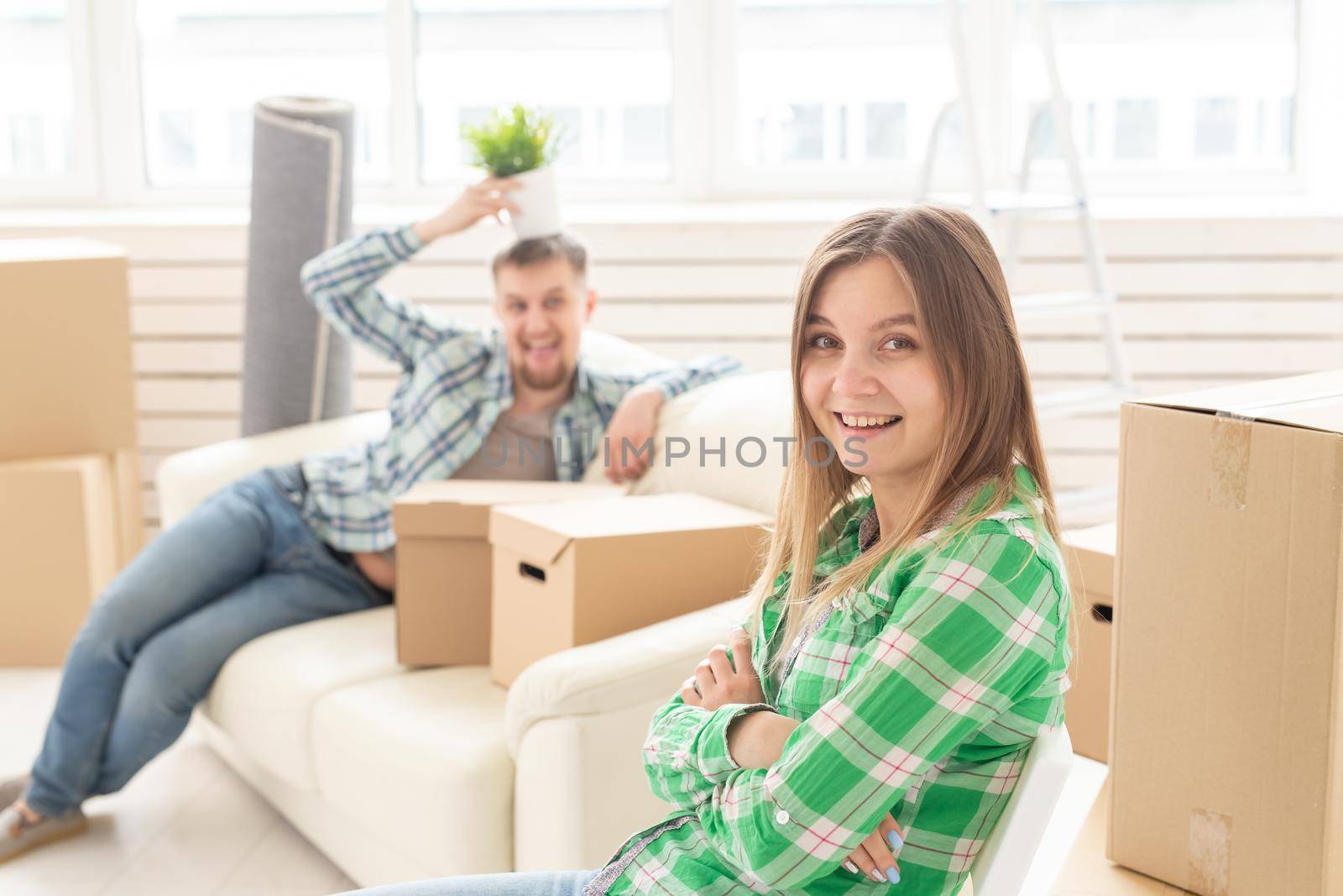 Positive smiling young girl sitting against her laughing blurred husband in a new living room while moving to a new home. by Satura86