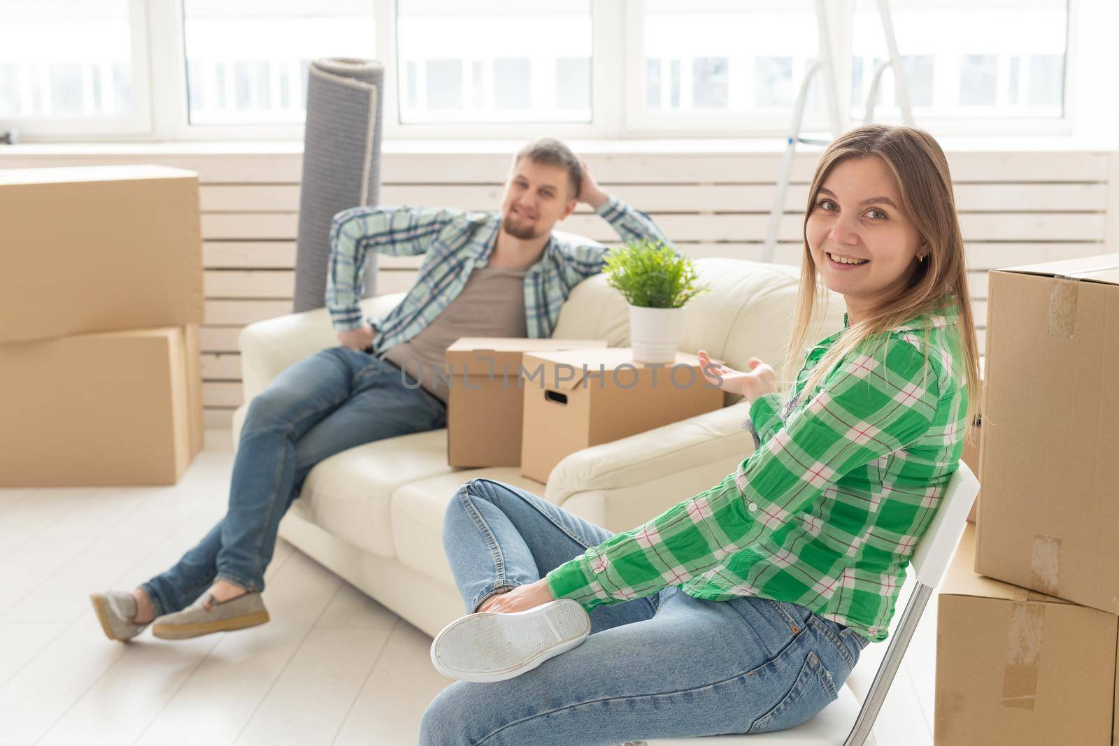 Positive smiling young girl sitting against her laughing blurred husband in a new living room while moving to a new home. The concept of joy from the possibility of finding new housing. by Satura86