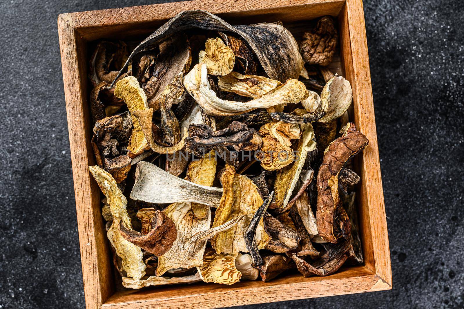 Boletus wild dried mushrooms in a wooden box. Black background. Top view.