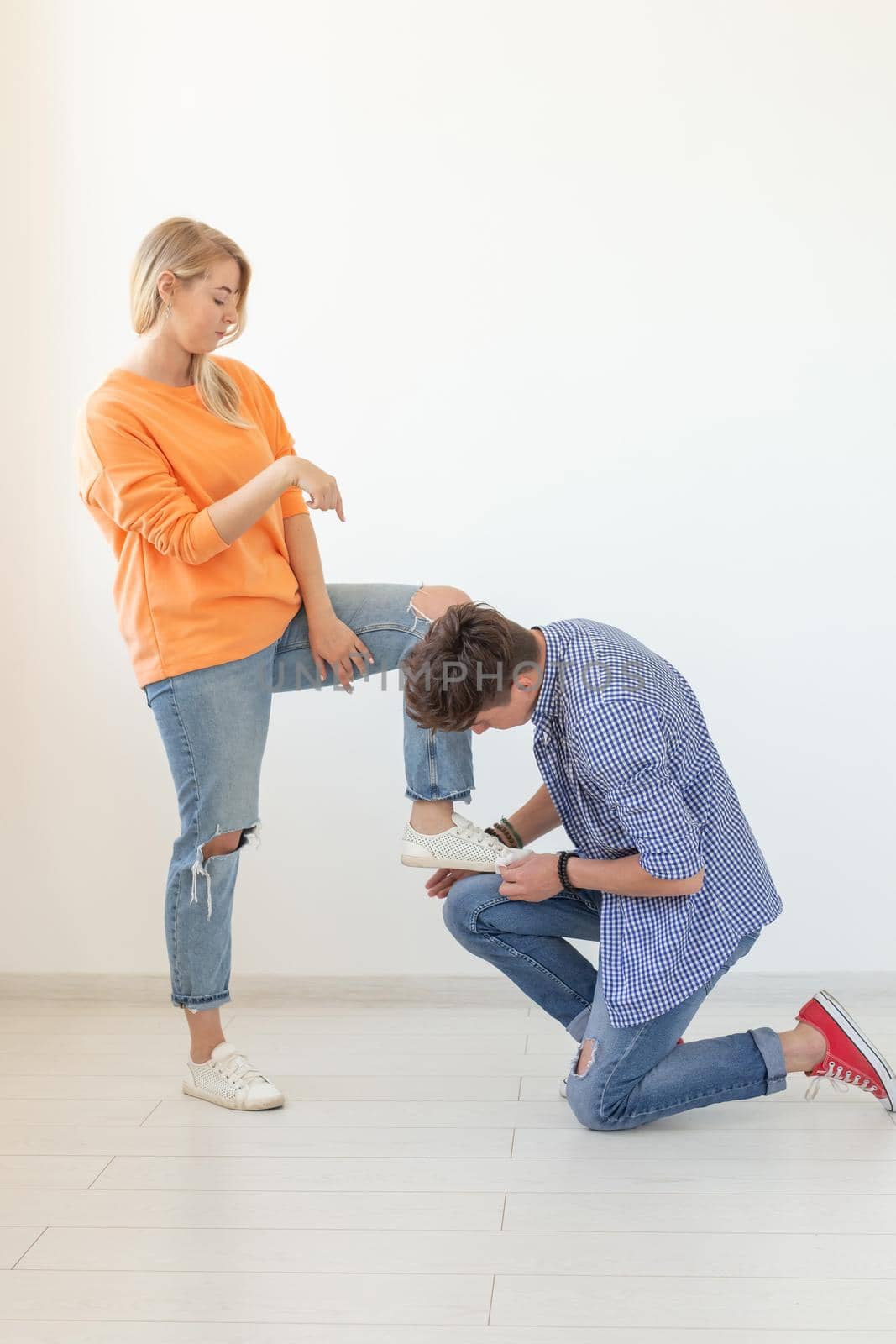 Young man tying shoelaces of his beloved woman posing on the white background. Concept of courtship and reverent relationships. Advertising space