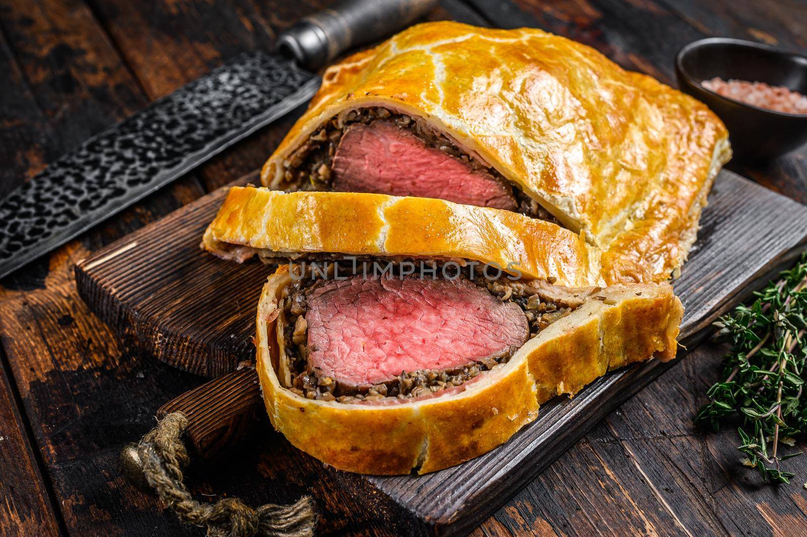 Homemade Beef Wellington puff pie with tenderloin meat on a cutting board. Dark wooden background. Top view.