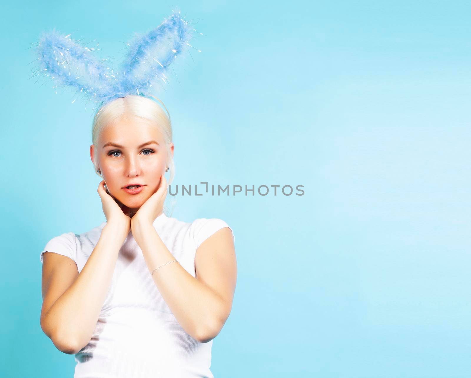 young pretty blond girl with rabbit ears posing cheerful on blue background, lifestyle people concept close up