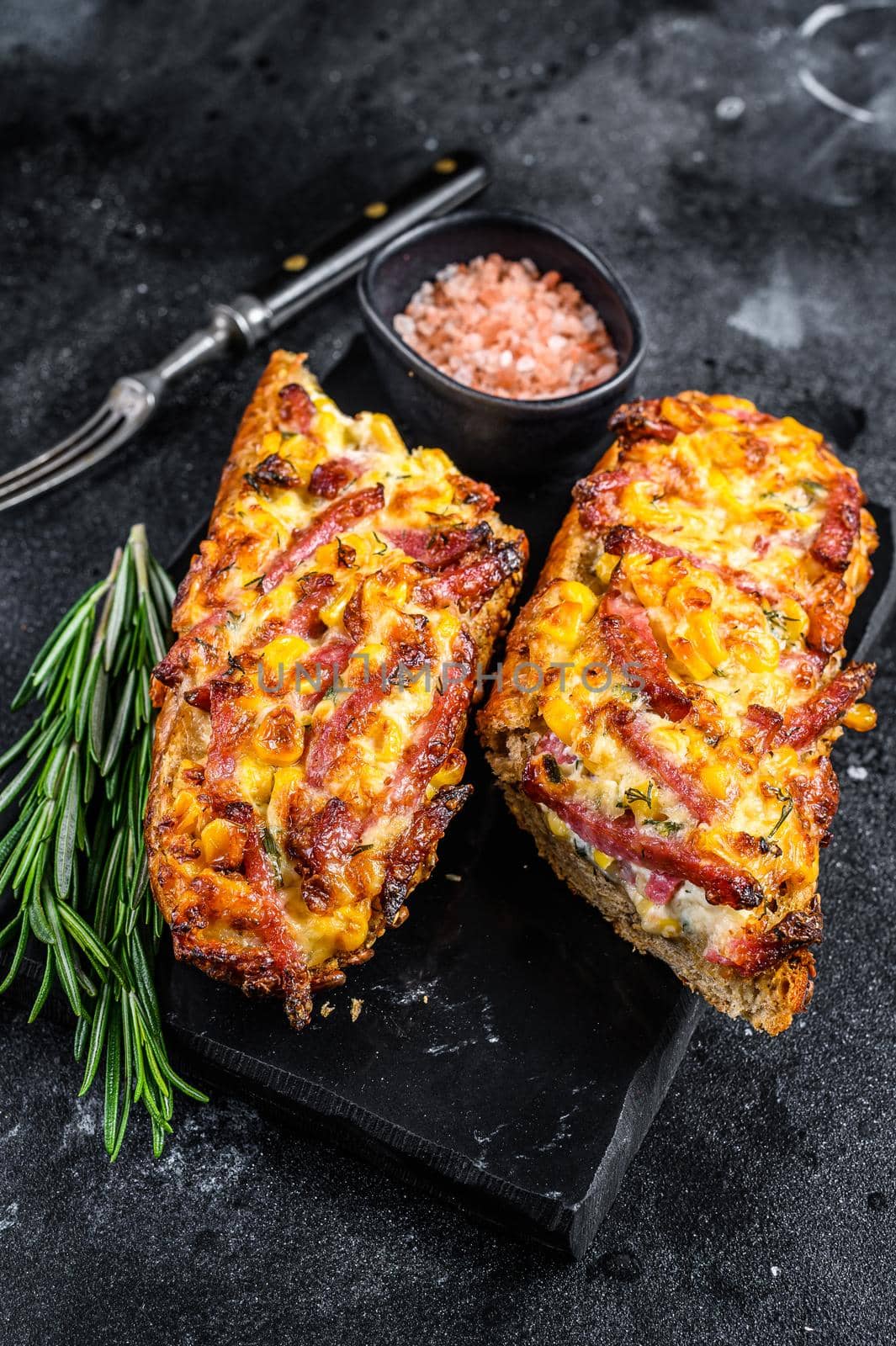 Hot baked open Baguette sandwich with ham, bacon, vegetables and cheese. Black background. Top view by Composter