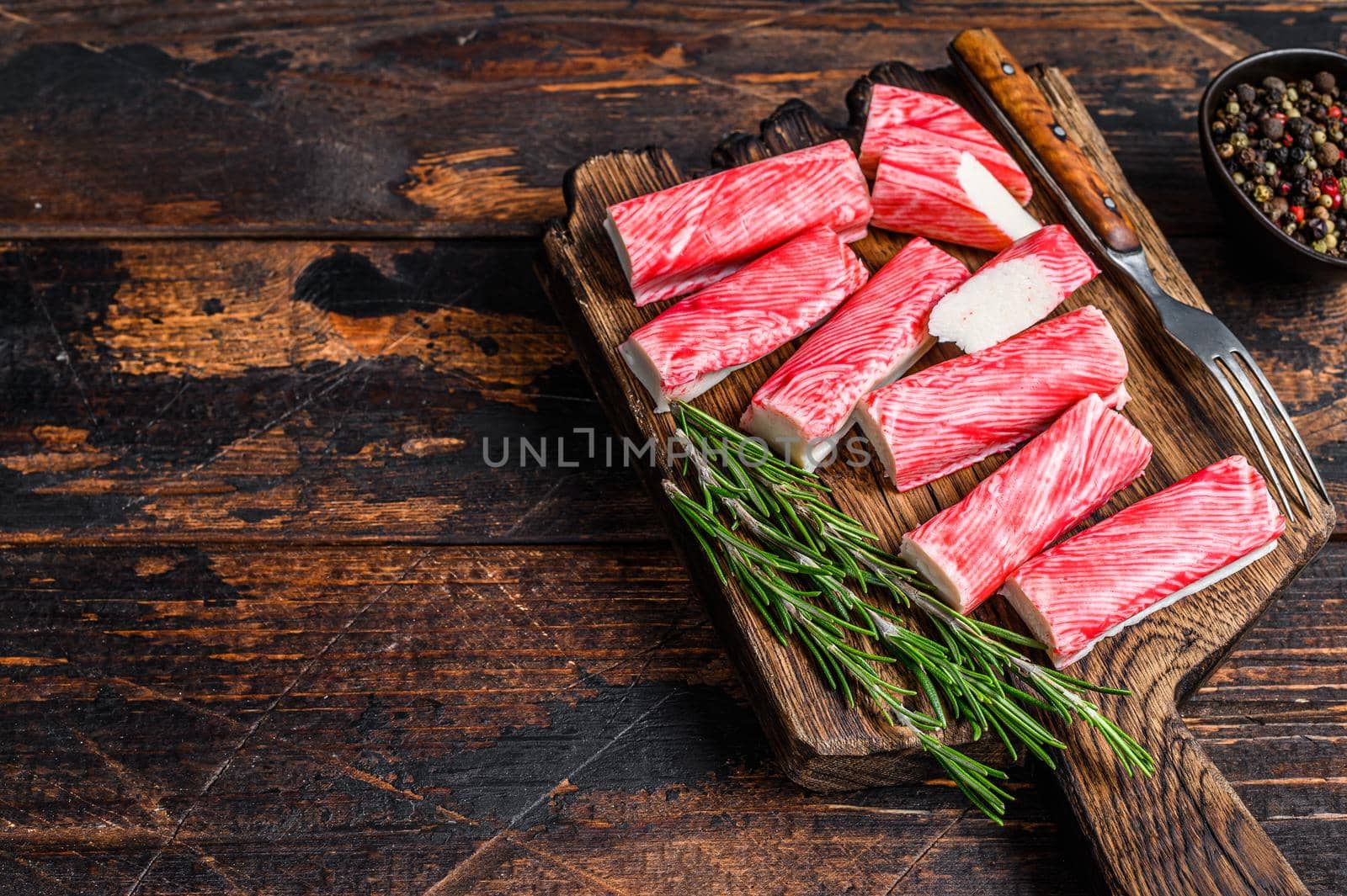 Sliced Crab surimi sticks on a wooden cutting board. Dark wooden background. Top view. Copy space by Composter