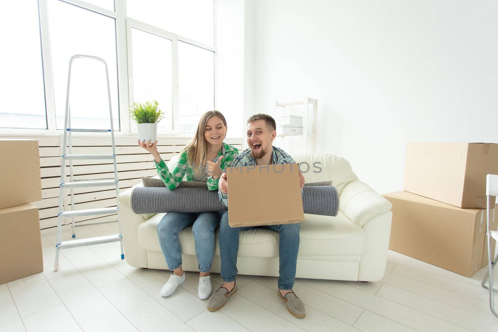 Cheerful joyful young couple charming girl and handsome man holding a box with things and a pot with a plant while moving to a new apartment. Housewarming and mortgage concept. by Satura86