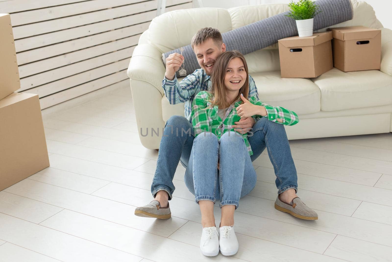 Young positive couple holding keys to a new apartment while standing in their living room. Housewarming and family mortgage concept