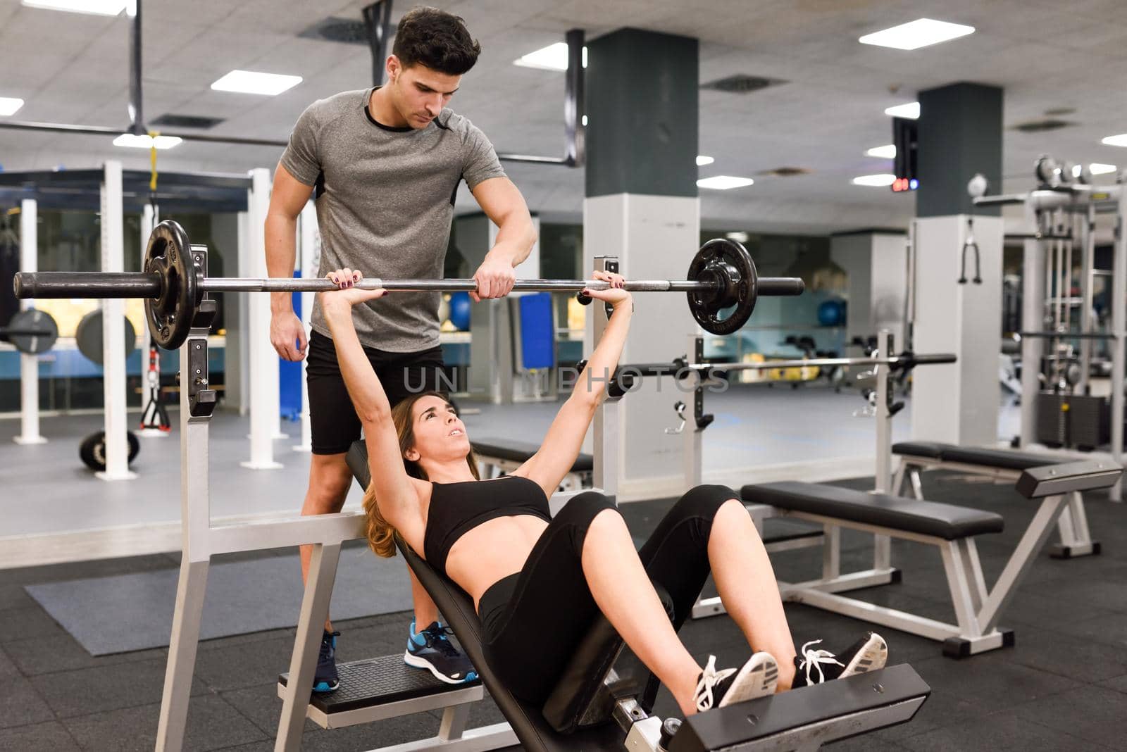 Personal trainer helping a young woman lift weights by javiindy