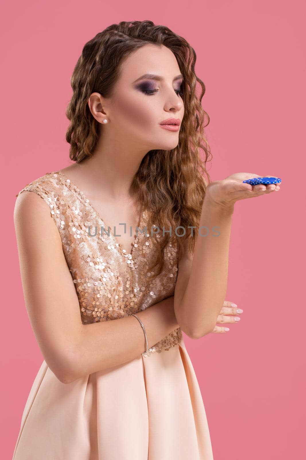 Beautiful young woman in dress with casino chips in the hands on pink background. Casino. Emotions. Gambling