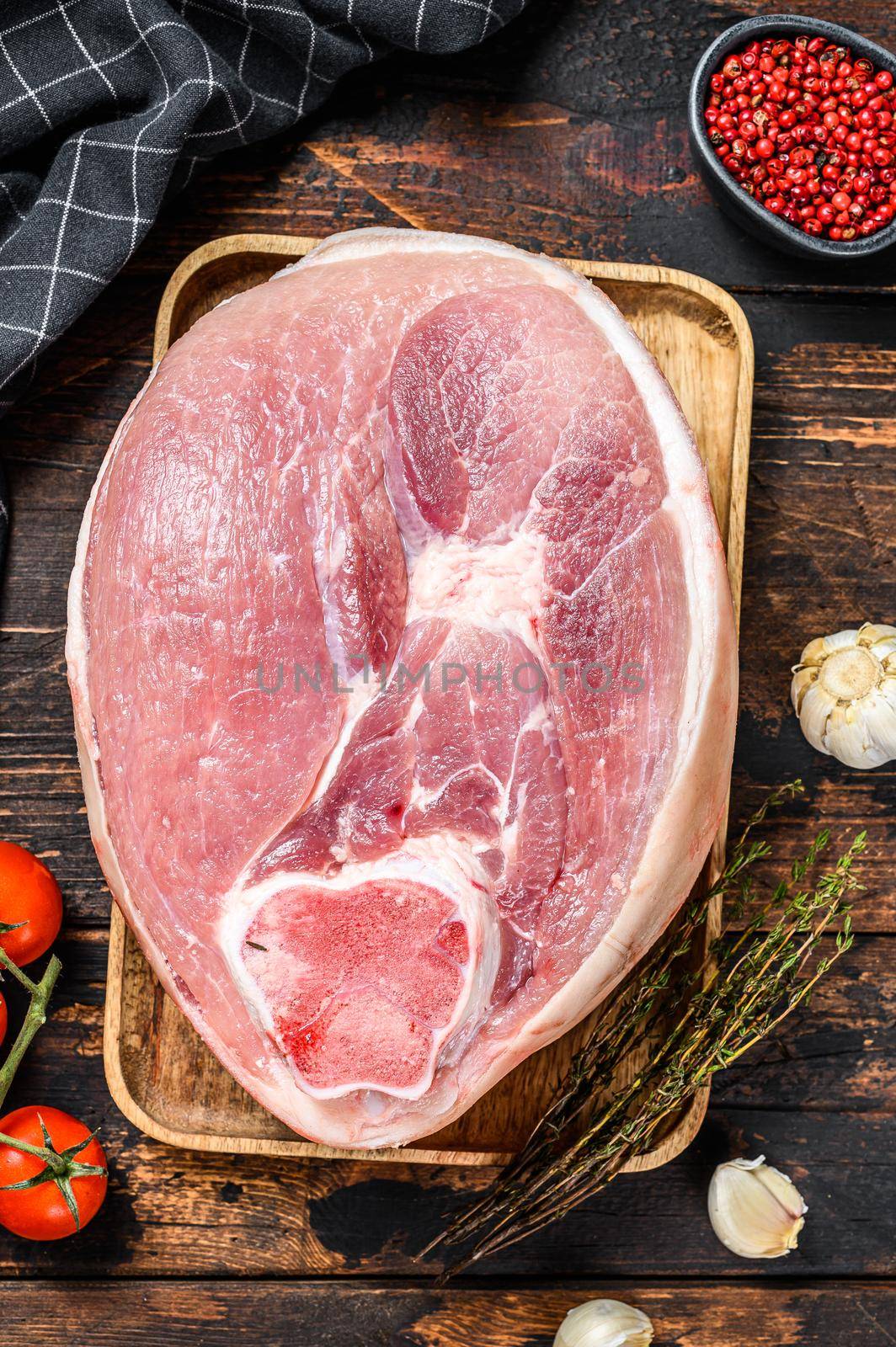 Cut of raw pork knuckle, leg on a cutting board. Farm fresh meat. Wooden dark background. Top view. by Composter