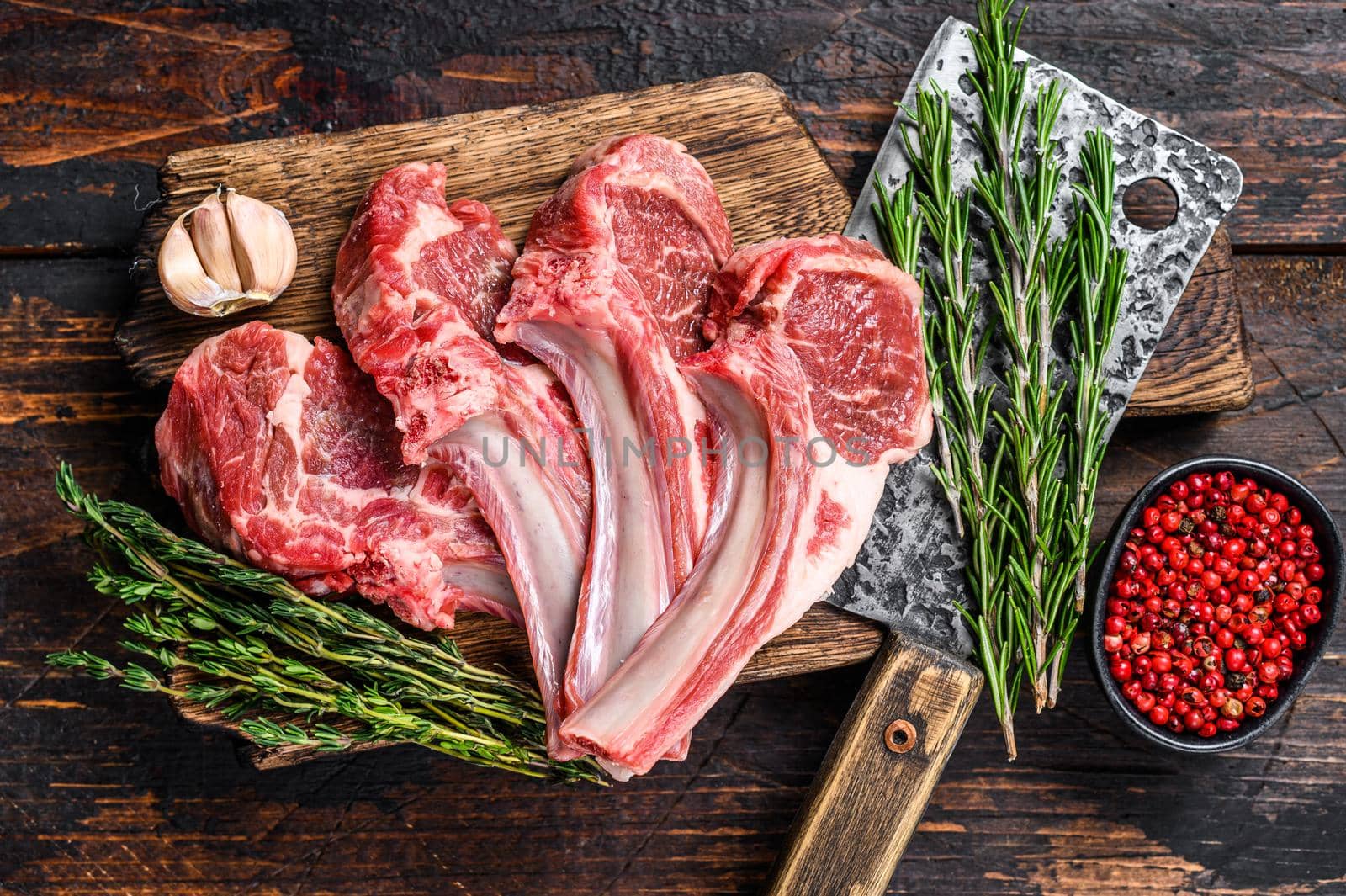 Lamb raw chops steaks on butcher cutting board. Dark wooden background. Top view.