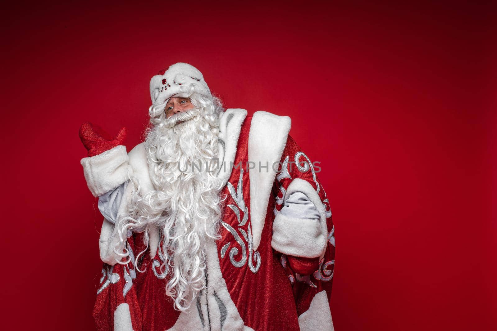 Stock photo of white-bearded Santa Claus in red and white costume dancing, moving arm up. Cutout on red background.