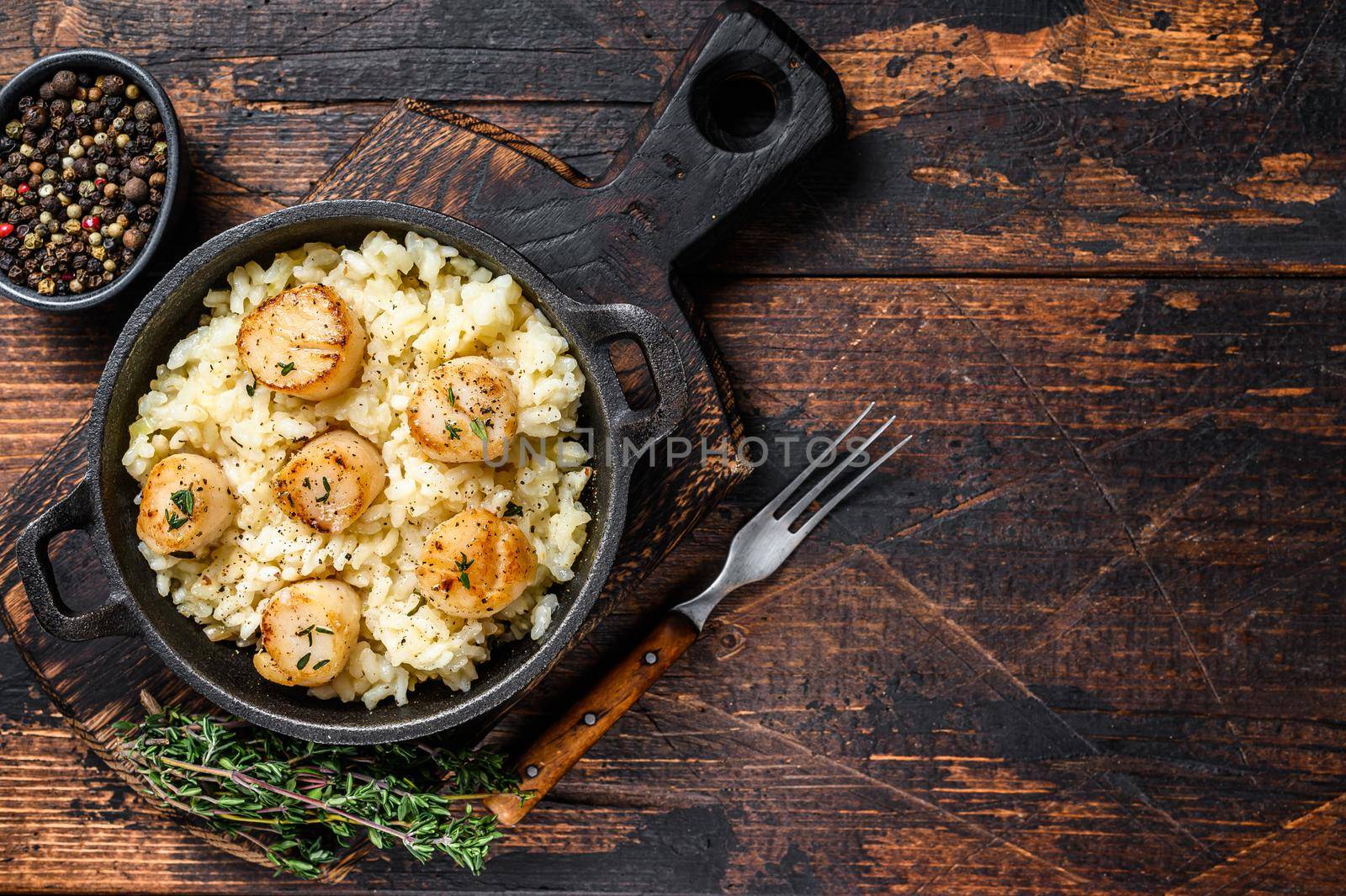 Seafood Risotto with Scallops in a pan. Dark wooden background. Top view. Copy space.