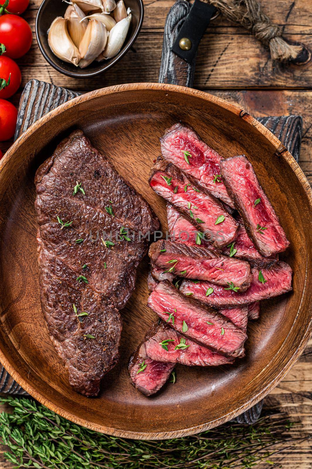 Grilled sliced top blade or denver beef meat steak in a wooden plate with herbs. wooden background. Top view.