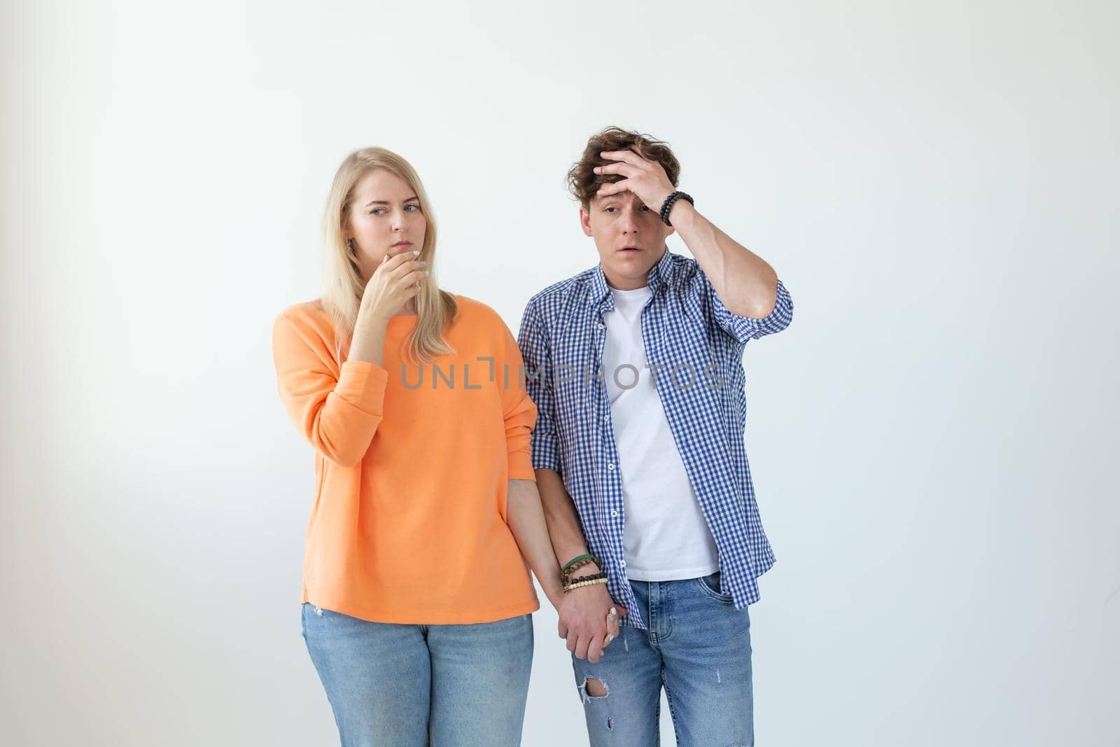 Young couple of students disgruntled boyfriend and tired young girlfriend posing on a white background holding hands. Concept of a crisis in relationships and the help of a psychologist