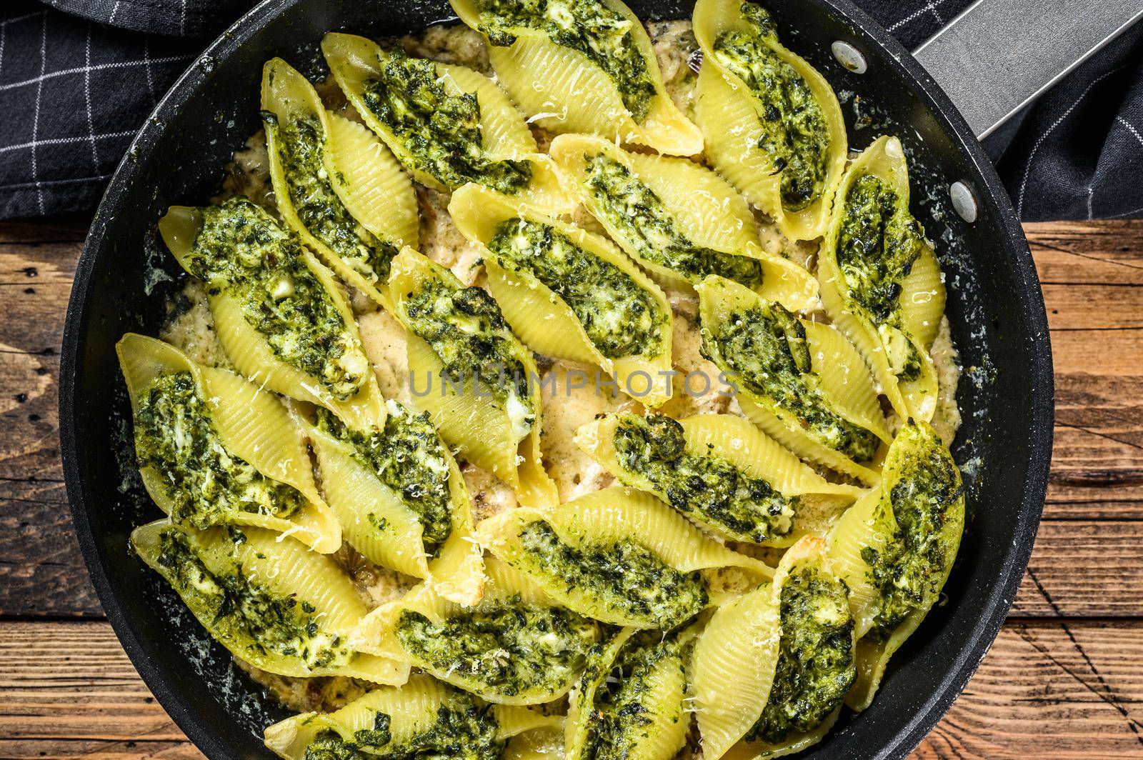 Pasta shells Conchiglioni stuffed with spinach and cheese baked with sauce in a pan. Wooden background. Top view by Composter